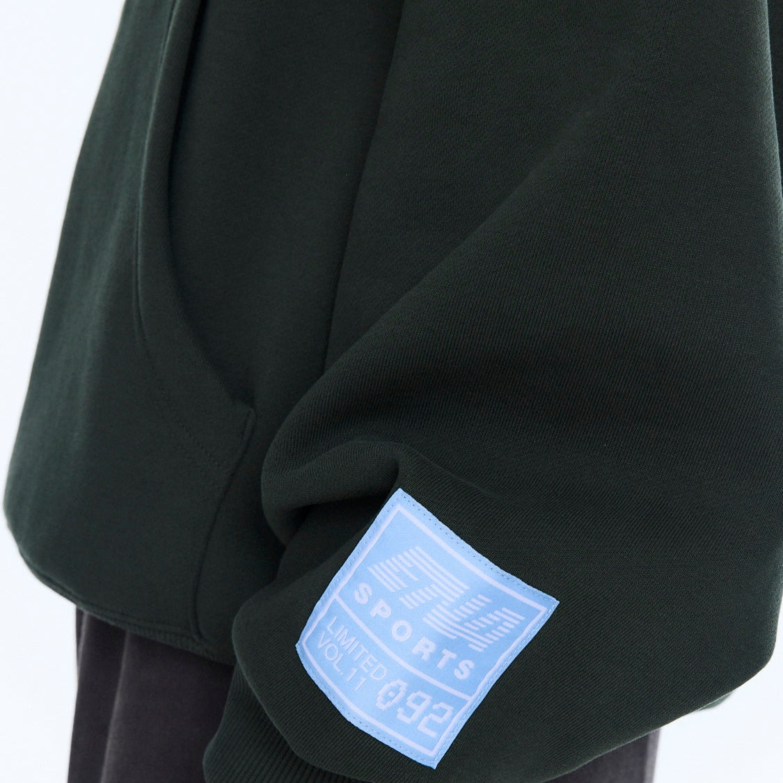 Detail shot of blue sports label patch on moss green hoodie sleeve cuff