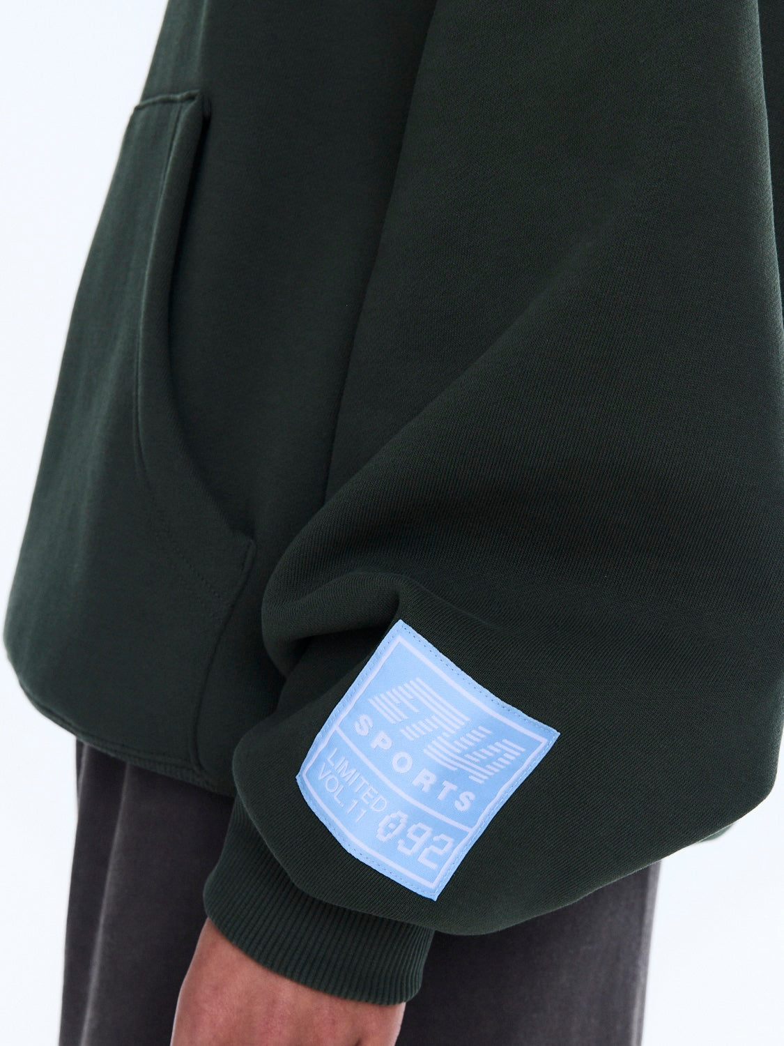 Detail shot of blue sports label patch on moss green hoodie sleeve cuff