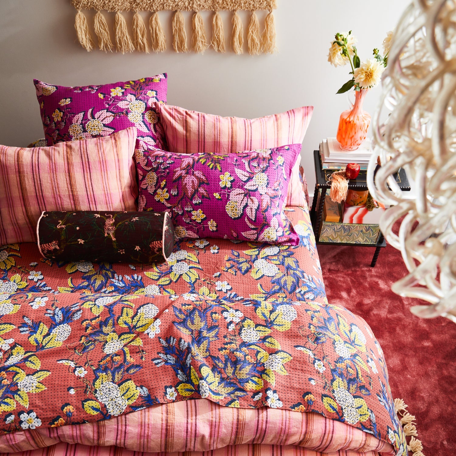 Bedroom styling of Andrea Bolster Cushion with pink striped pillows and floral bedding arrangement