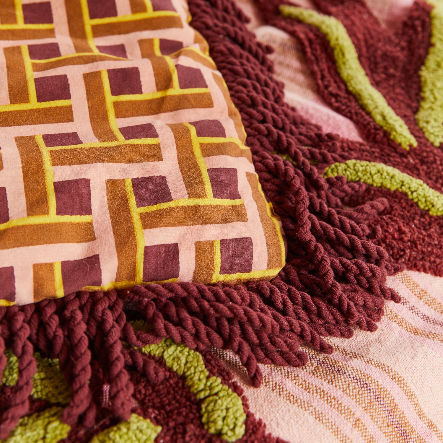 Aneta Tufted Blanket displayed on bed with geometric pattern panel and burgundy fringe border detail