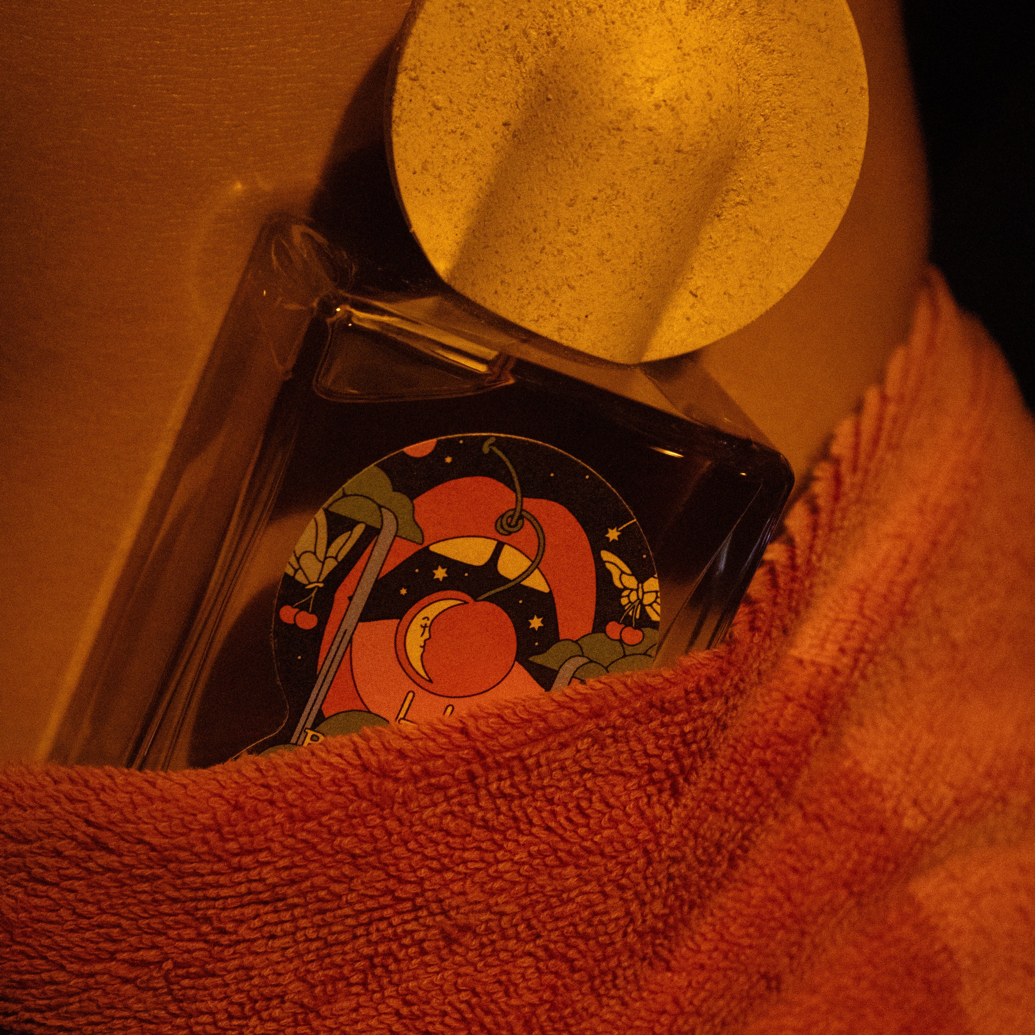 Close-up of Bain De Minuit perfume nestled in coral textured towel with speckled cap visible