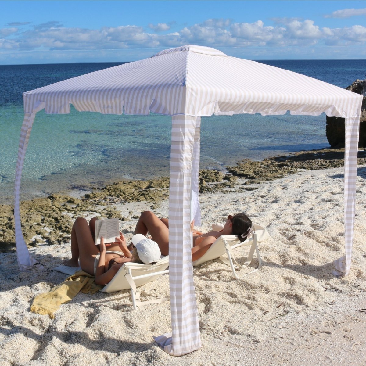 Sunnylife Casa Stripe beach cabana set up on sandy beach with blue ocean backdrop