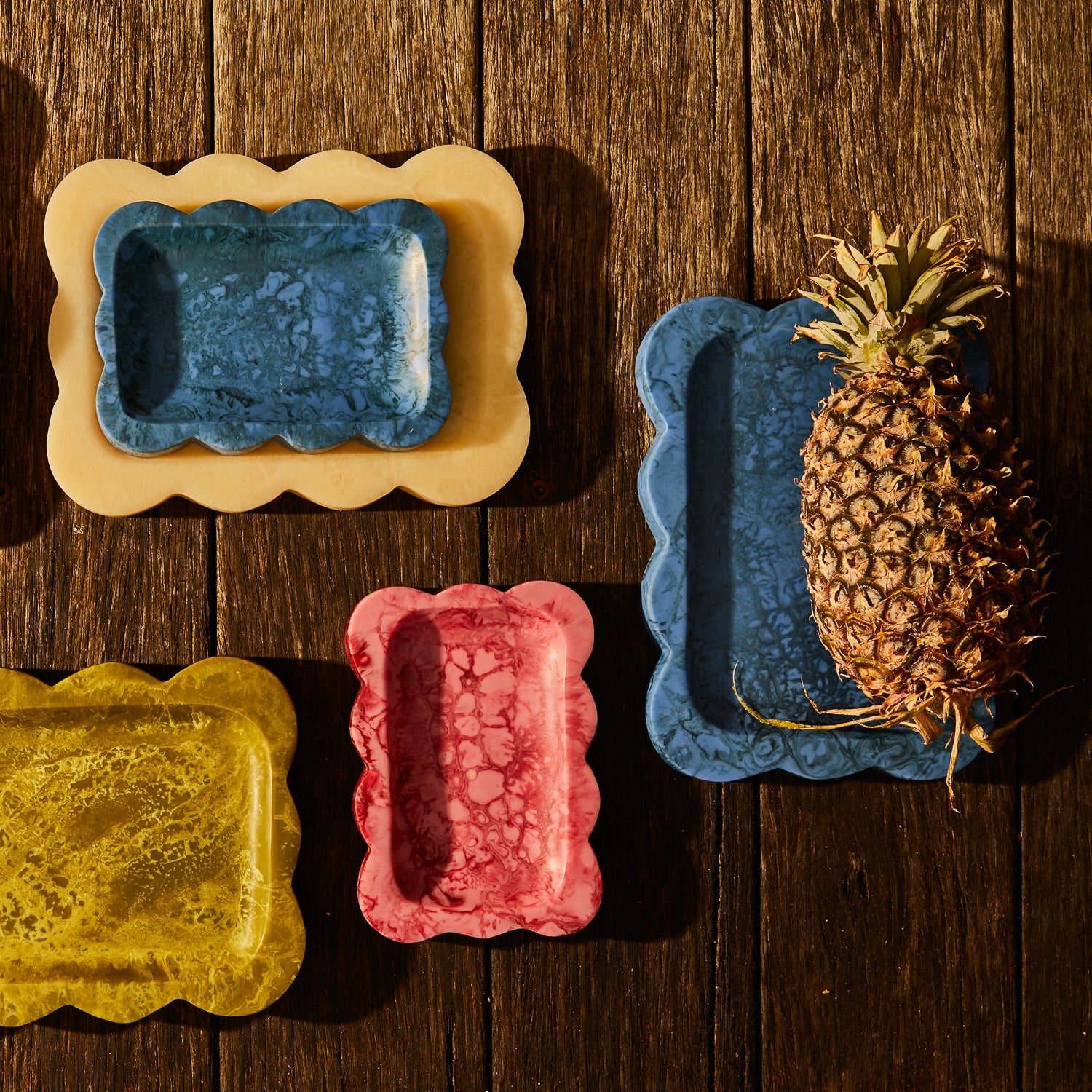 Crimson marbled resin small tray with scalloped edge, top-down view styled with colorful trays on wood surface