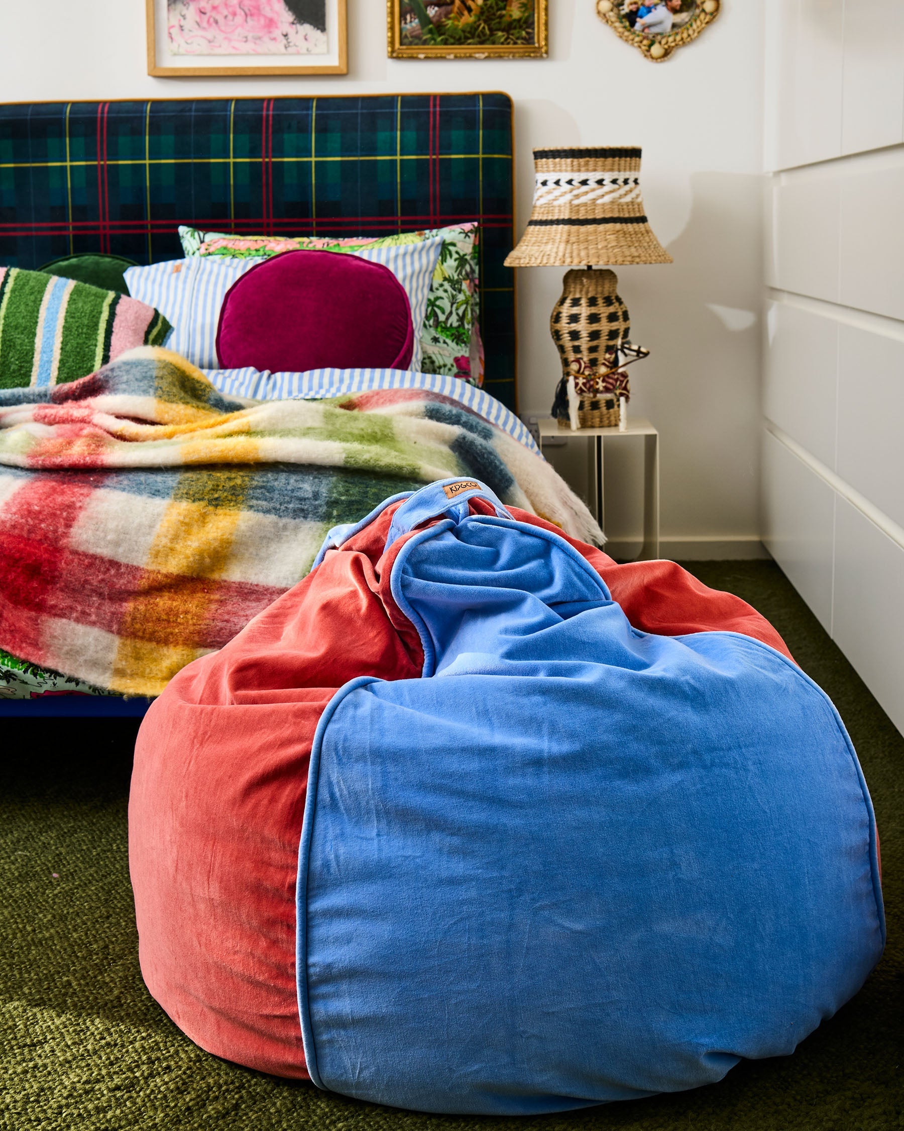 Blue Robin velvet beanbag positioned next to colorful bedroom with plaid headboard and bedding