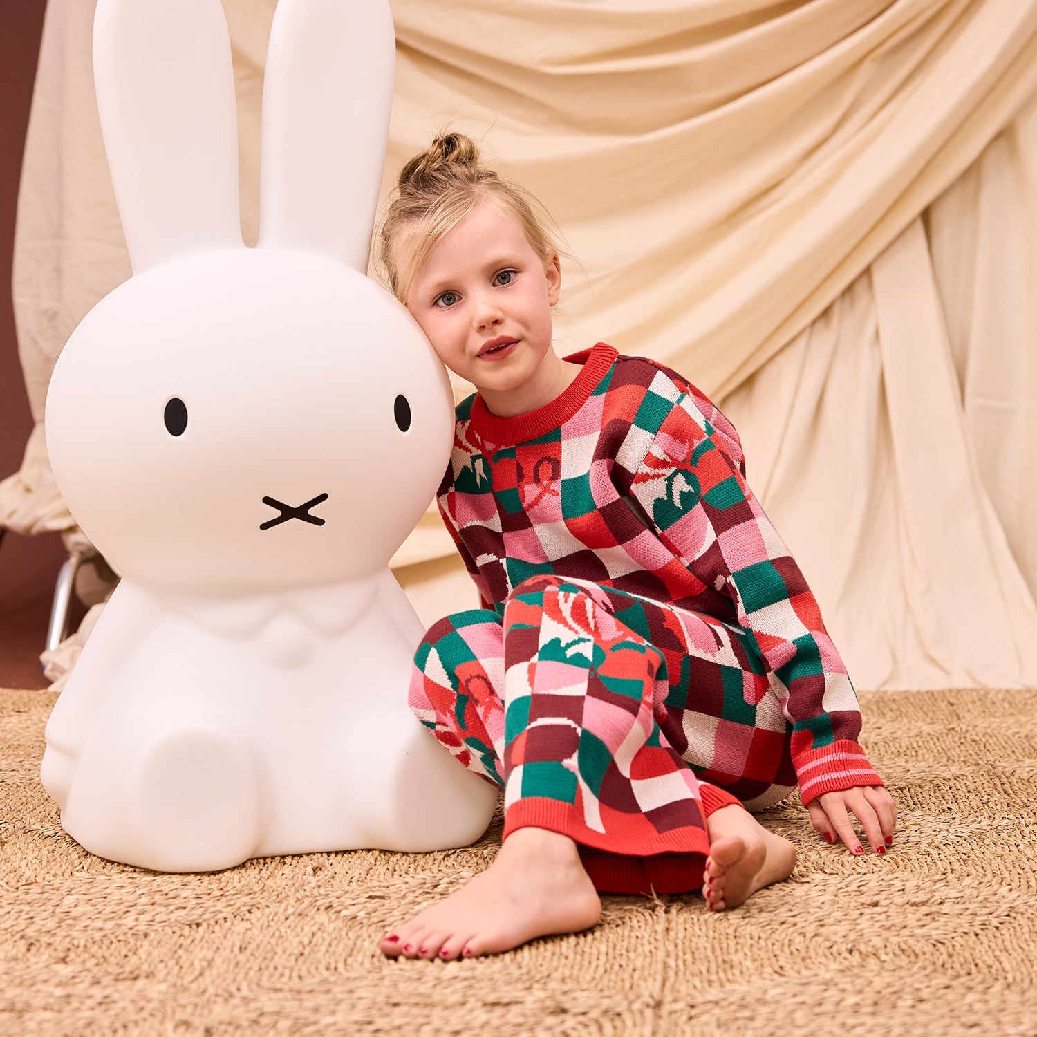 Child wearing matching Bodhi Kids knit pajama set with colorful checkered pattern and red ribbed cuffs