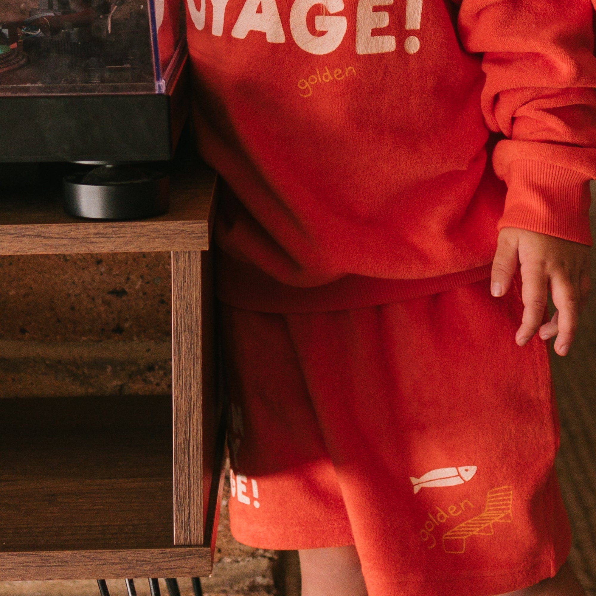 Child wearing red Bon Voyage outfit showing Golden Children branded shorts and sweatshirt