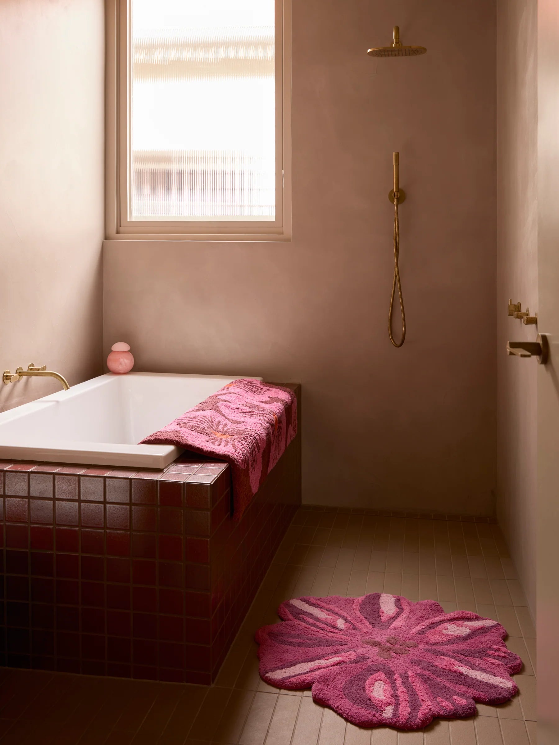 Jardin Pink Long Bath Mat by Bonnie & Neil displayed in a pink rendered bath room with gold shower fittings and red coloured bath