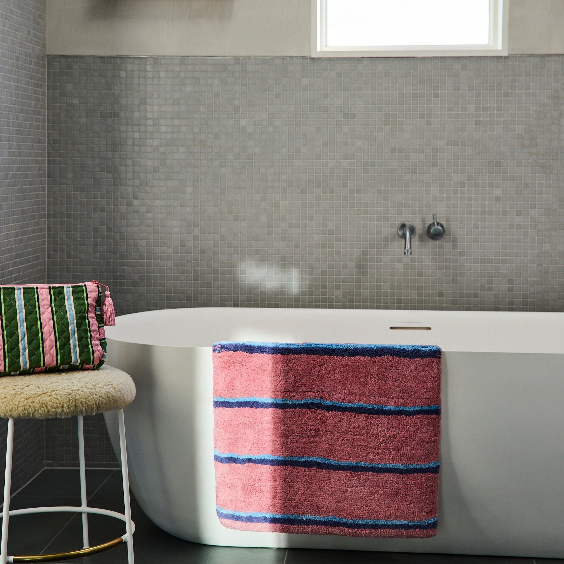 Cactus Stripe toiletry purse positioned on bathroom stool beside white bathtub in modern tiled bathroom setting
