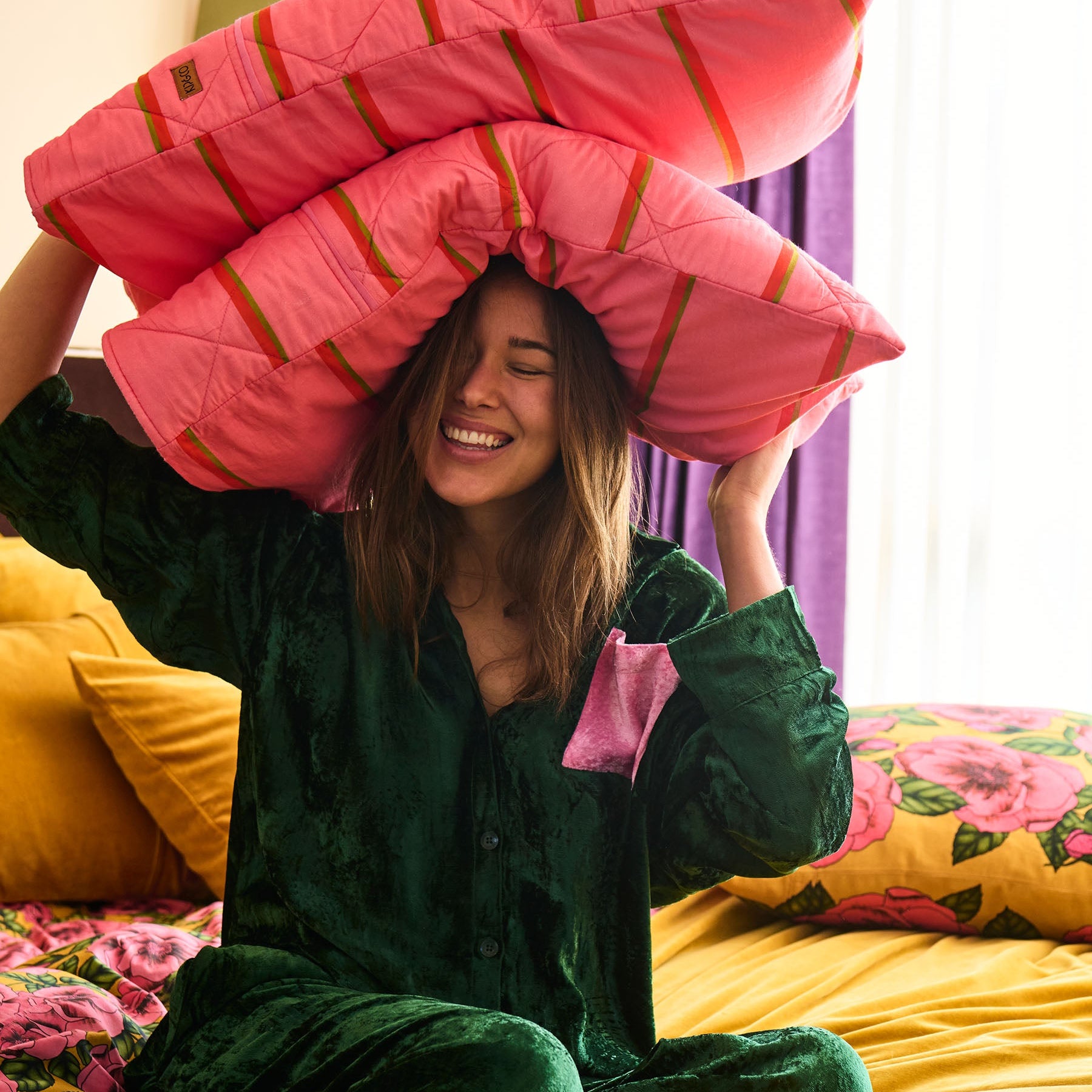 Model holding pillow wearing Candy Pine velvet pyjama set showing playful bedroom styling