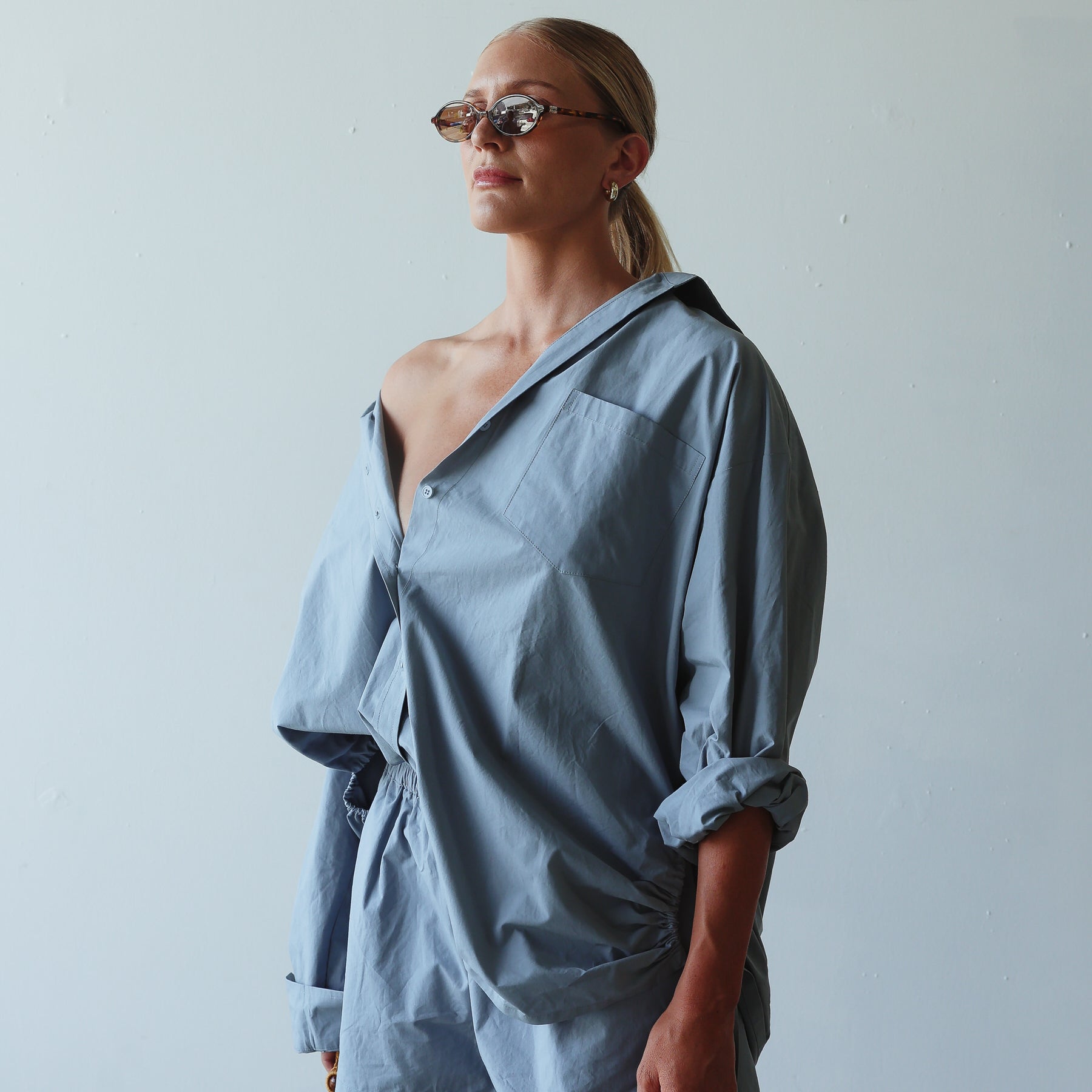 Woman wearing a blue outfit with sunglasses against a plain background