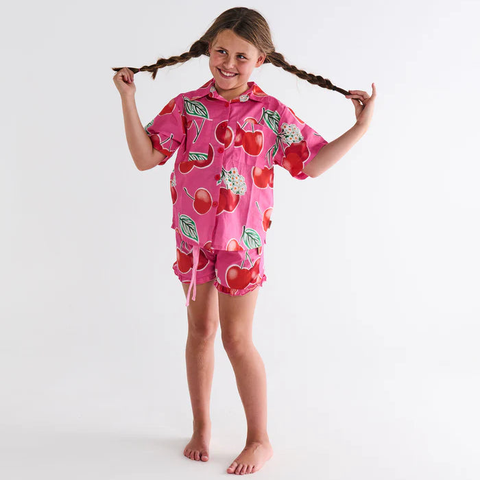 girl wearing Cherry Blossom Kids Organic Cotton Short Sleeve Shirt & Short Pyjama Set by Kip & Co - pink pj's with red cherries