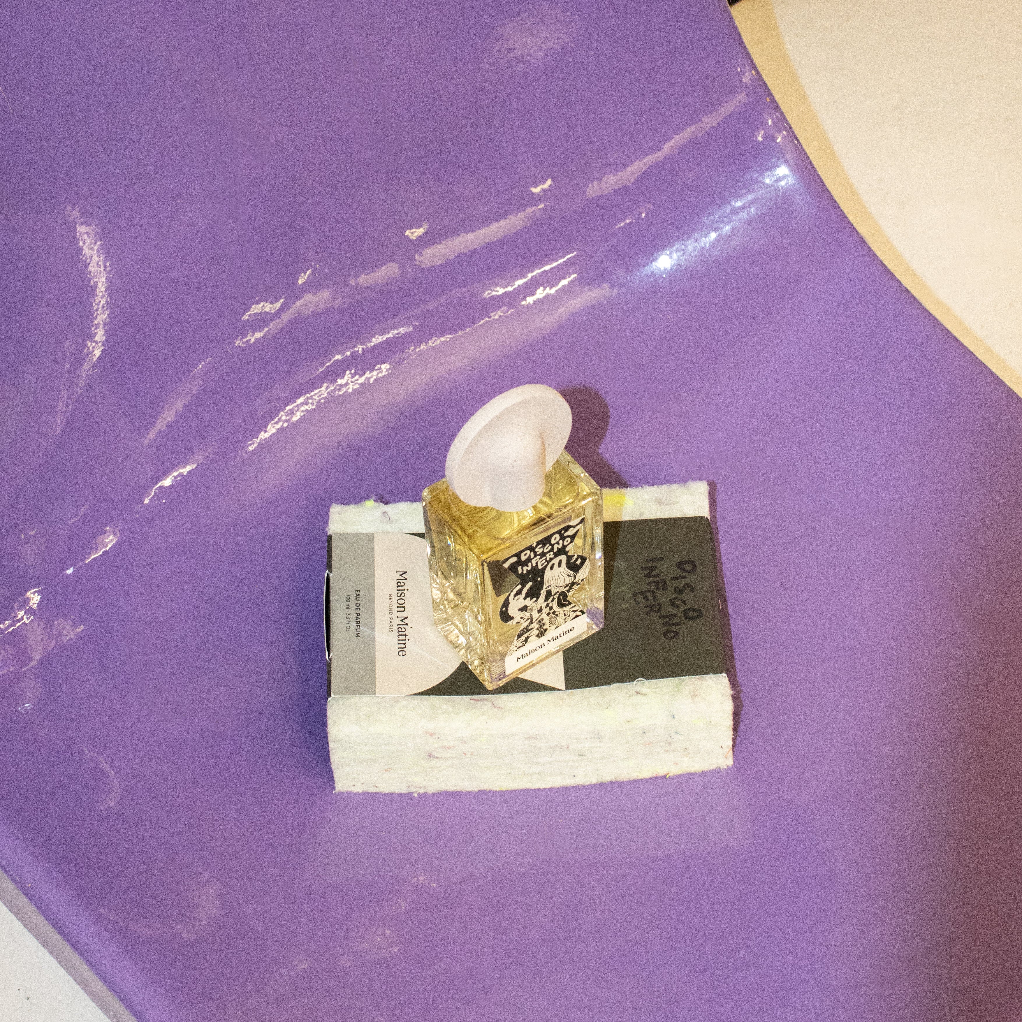 Disco Inferno perfume positioned on white packaging box against glossy purple surface with reflections