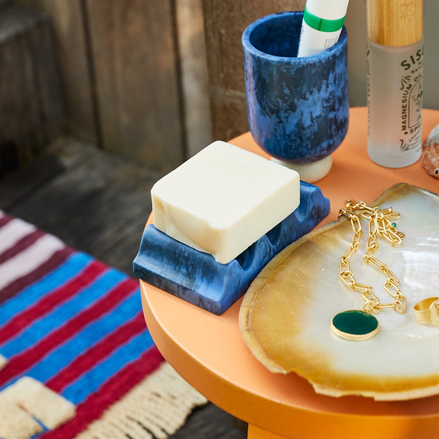 Azure marbled wave soap dish with a bar of soap on an orange side table, styled with a toothbrush cup and jewellery