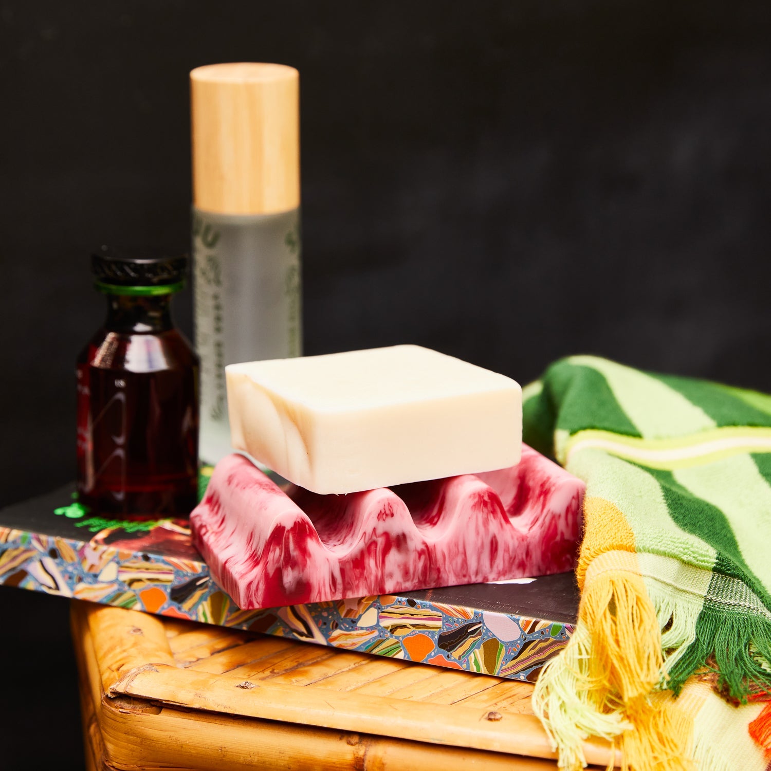 Crimson marbled wave soap dish holding a bar of soap, styled on a bamboo surface with bathroom accessories