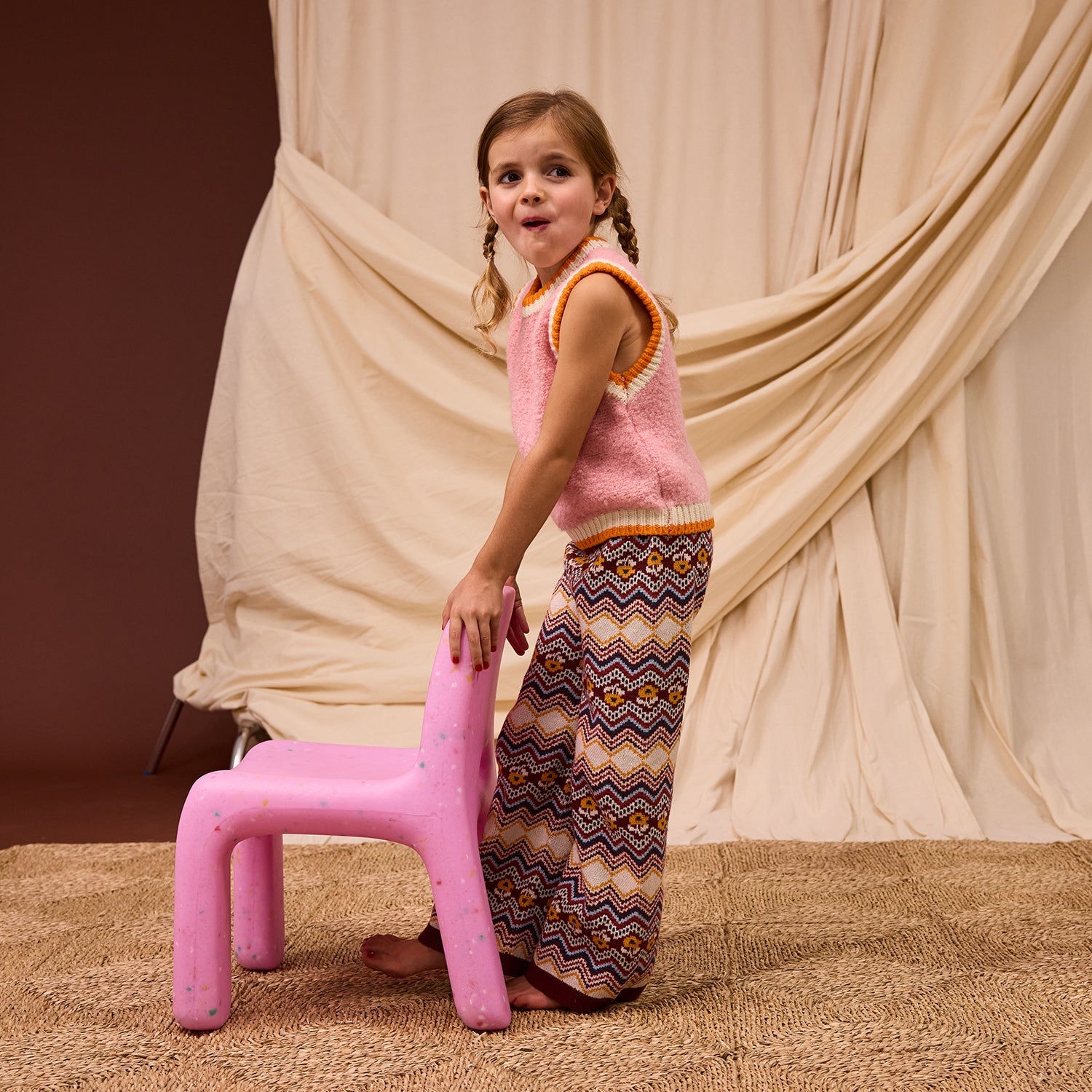 Side angle of blush pink Kids Knit Vest displaying relaxed fit and striped edge finishing
