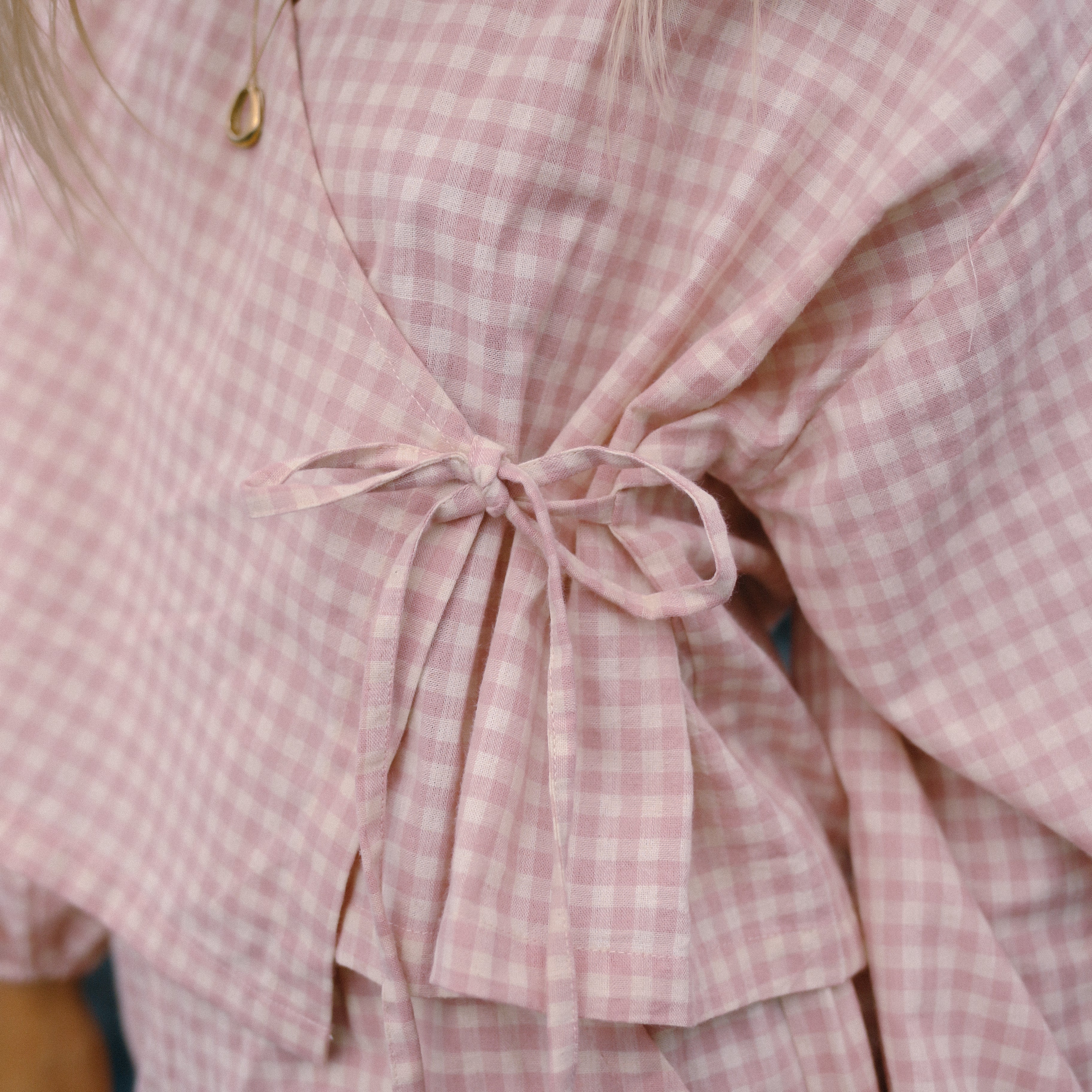 Close-up of a pink gingham wrap top with a tie waist. Made from linen and cotton
