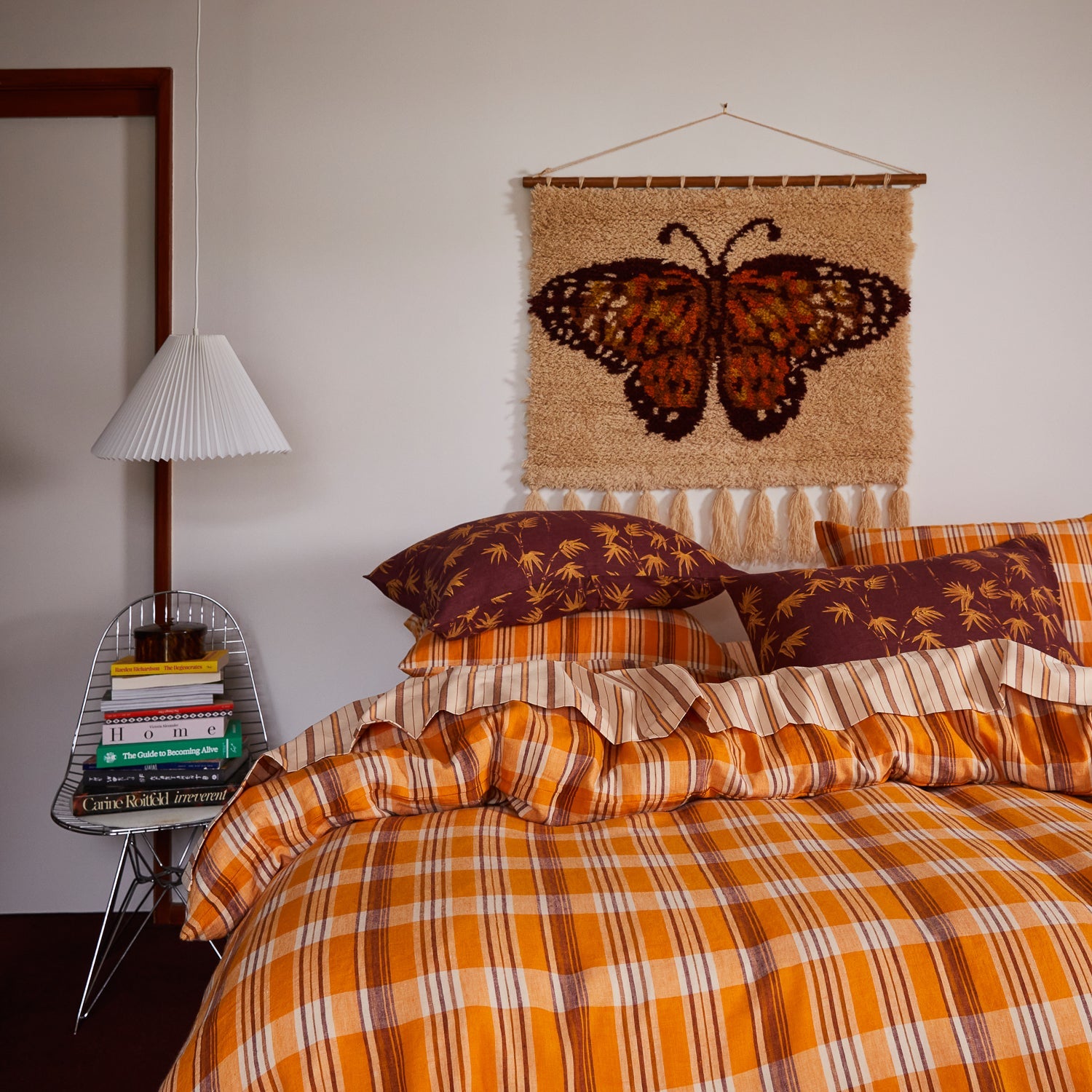 Emilia Wall Hanging above bed with orange plaid bedding showing butterfly tapestry with wooden dowel rod