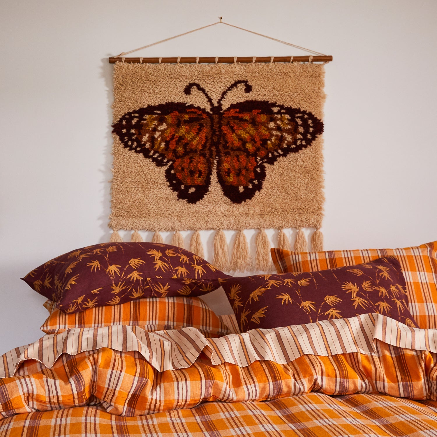 Wall hanging with butterfly design above bed showing cream background and tassel detail in bedroom setting