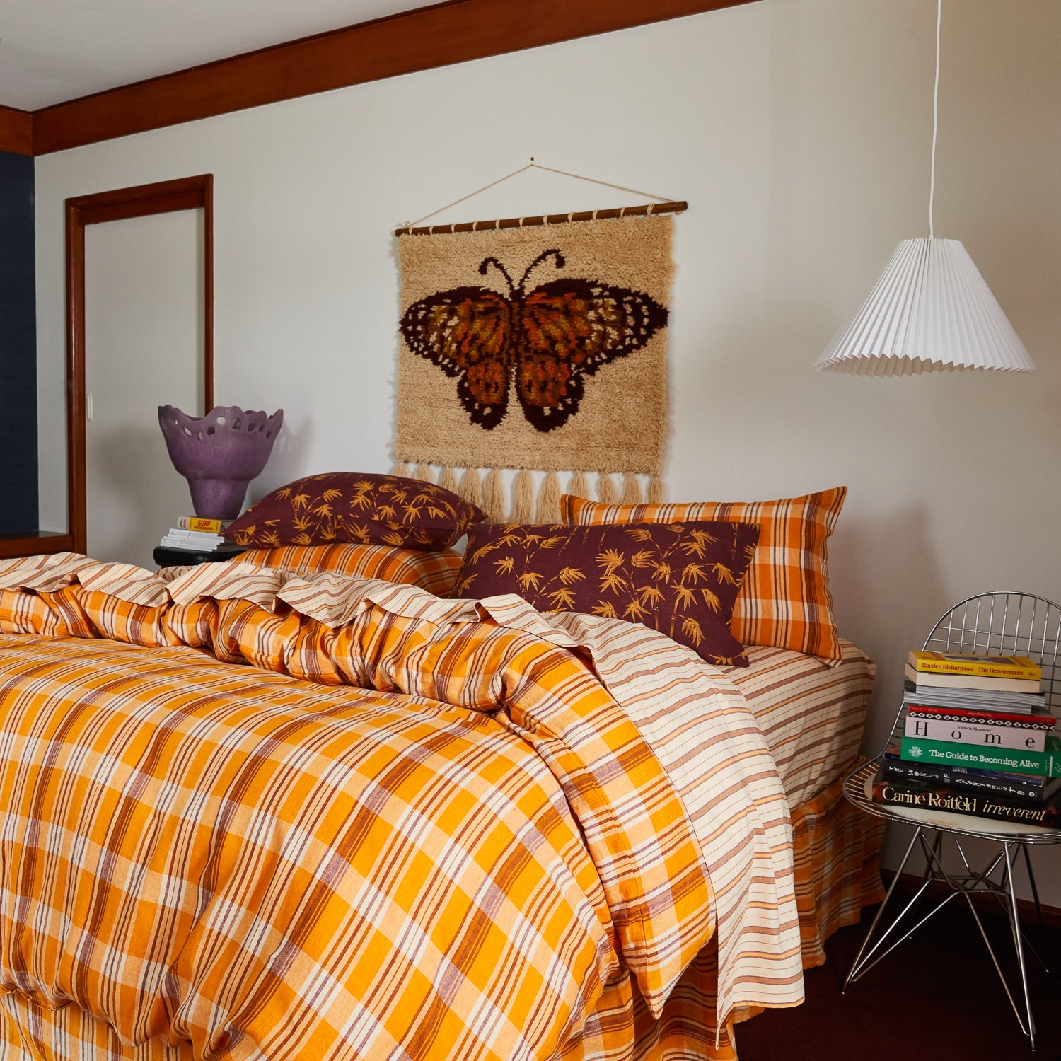 Emilia Wall Hanging in bedroom corner with orange plaid bedding and burgundy butterfly motif on textured fabric