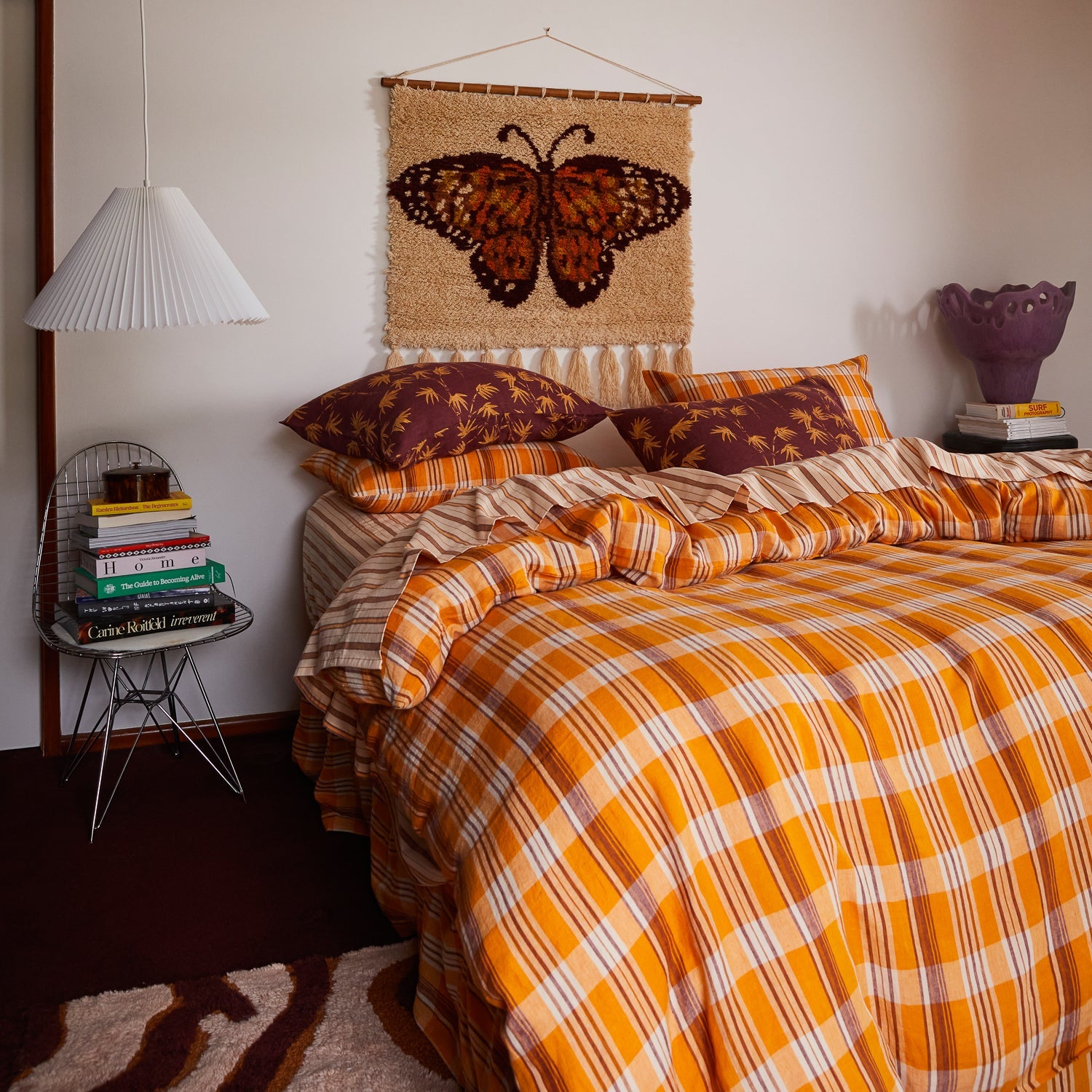 Butterfly wall hanging above bed with brown pillows showing orange and burgundy tapestry with cream fringe