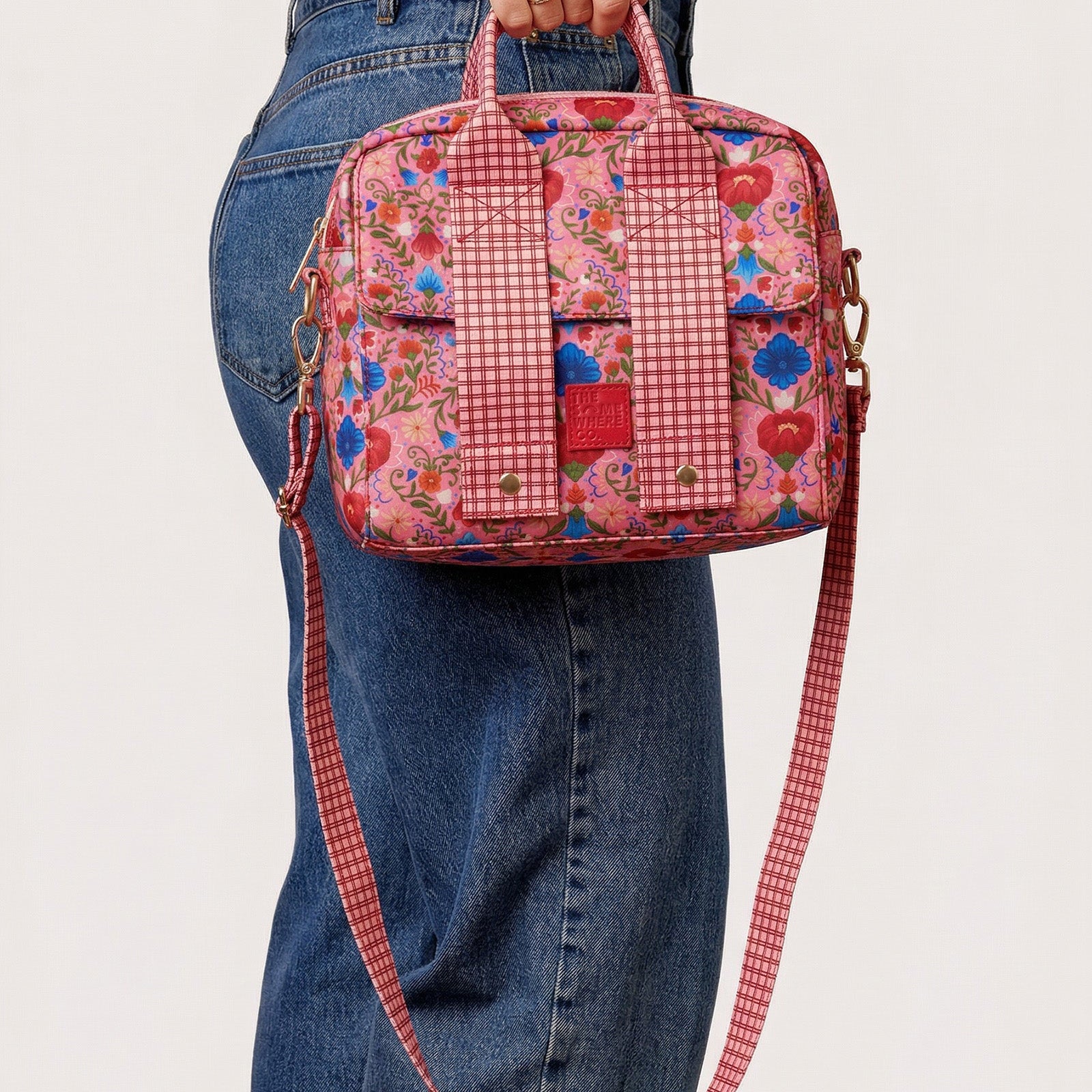 Fable lunch tote carried by hand showing floral print and gingham crossbody strap detail