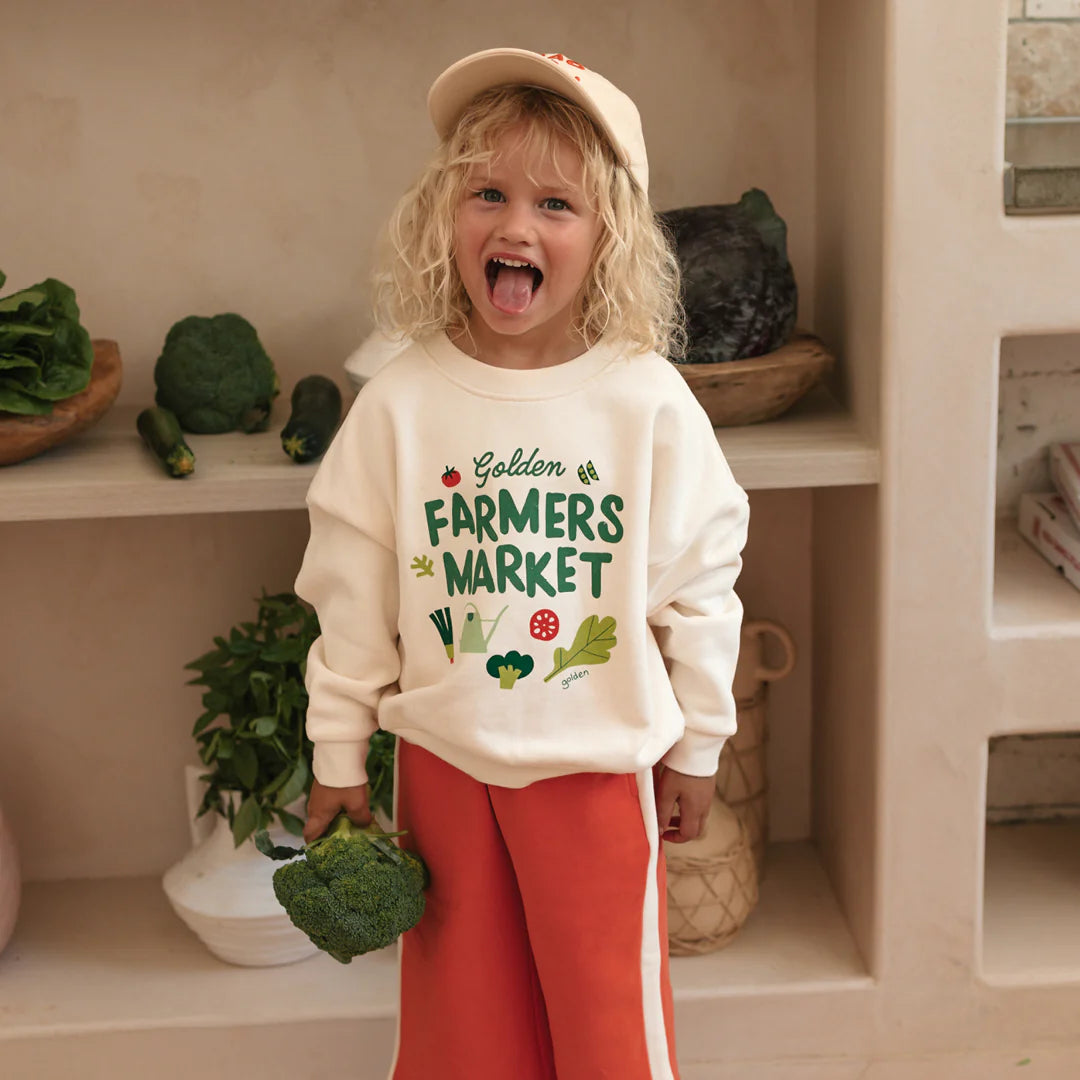 Little girl wearing the Farmers market Sweater Buttercream by Golden Children and wearing the ciao tutti red pants