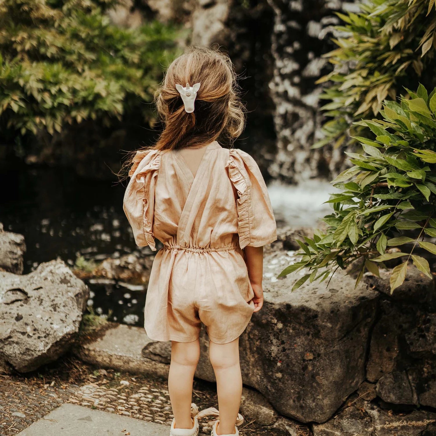 Girl wearing Femmie Playsuit by Donsje in a pink / beige colour with ruffle sleeves and open back