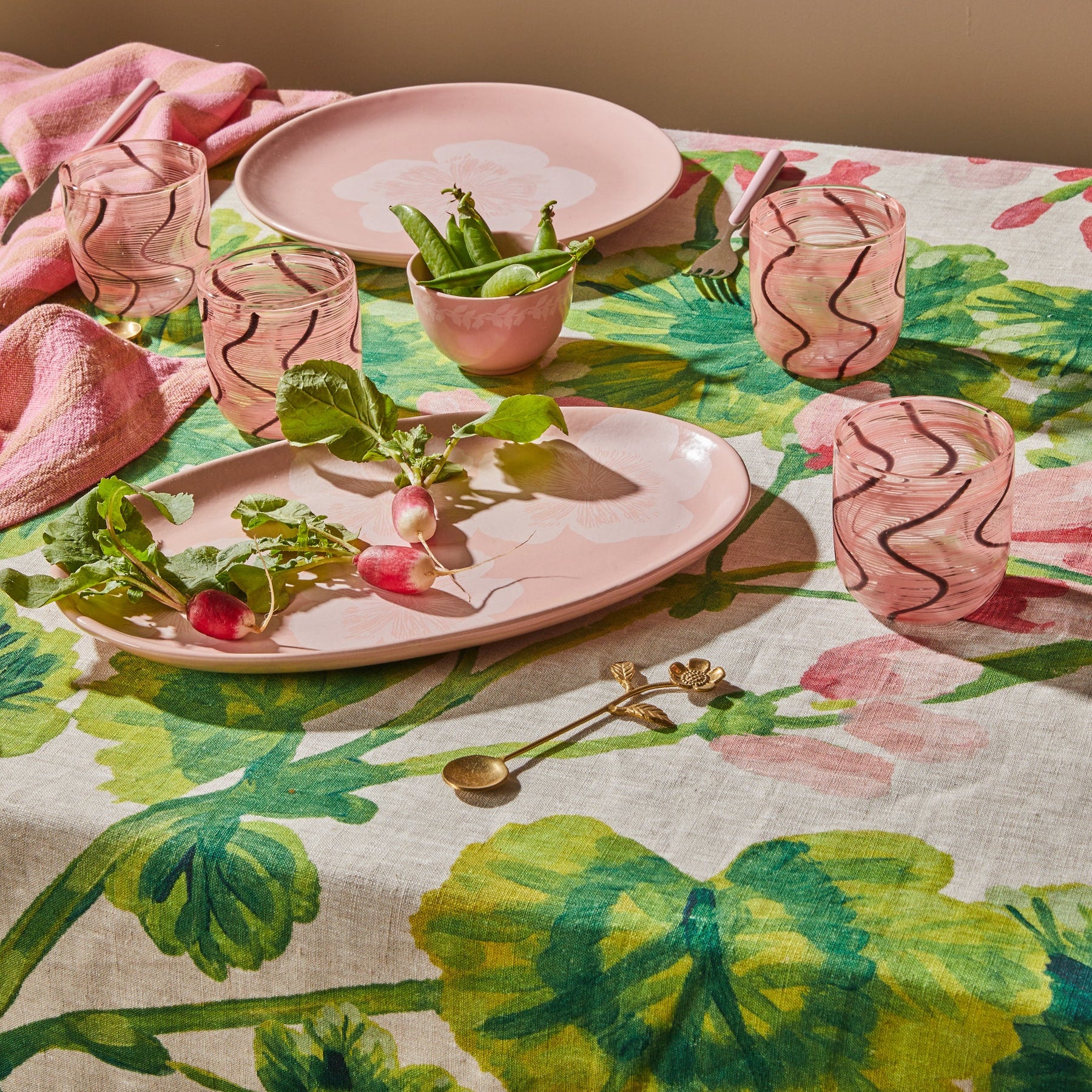 Table setting with pink plates, cups, and napkins on a floral tablecloth by Bonnie & Neil