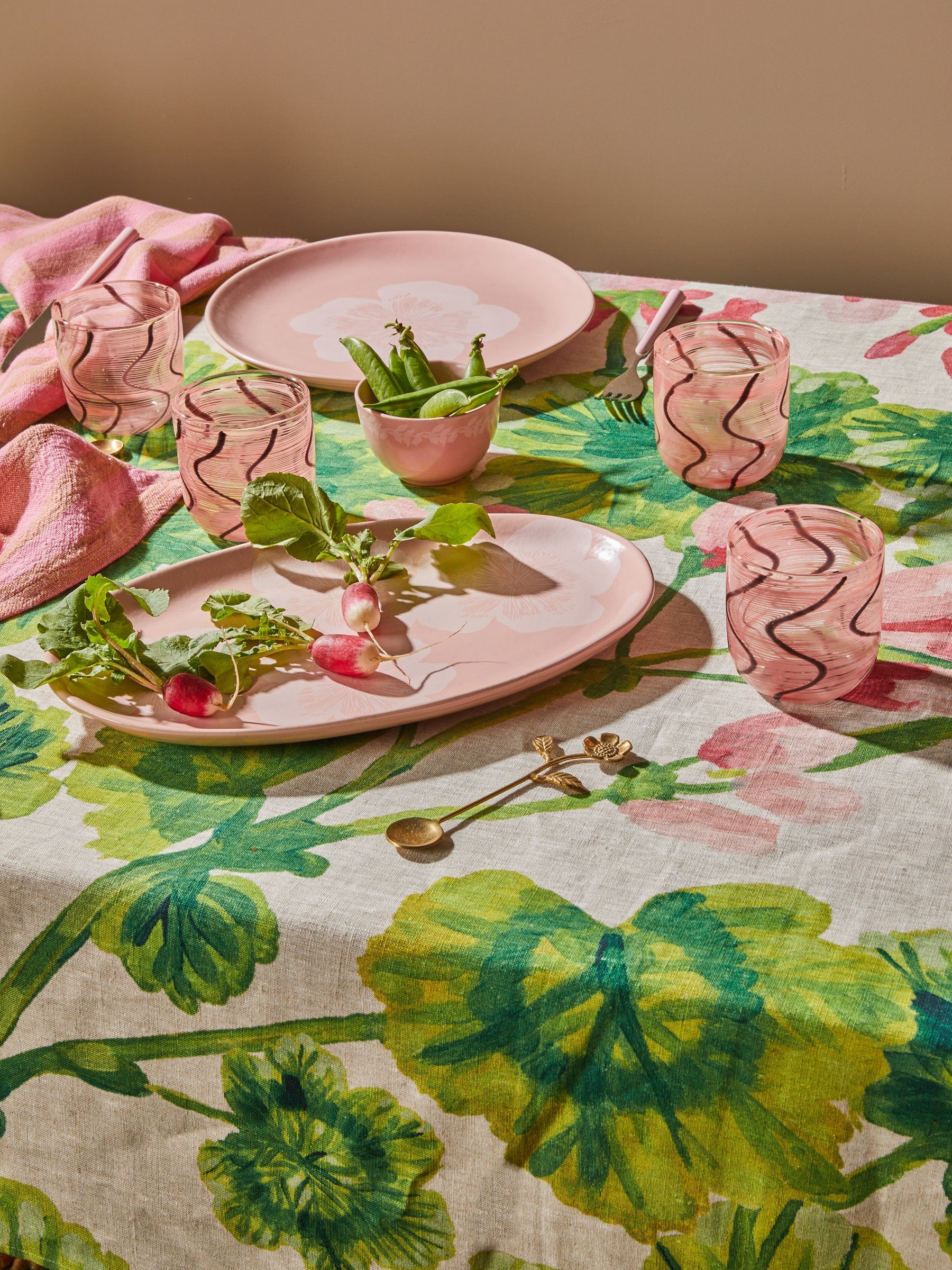 Table setting with pink plates, cups, and napkins on a floral tablecloth by Bonnie & Neil
