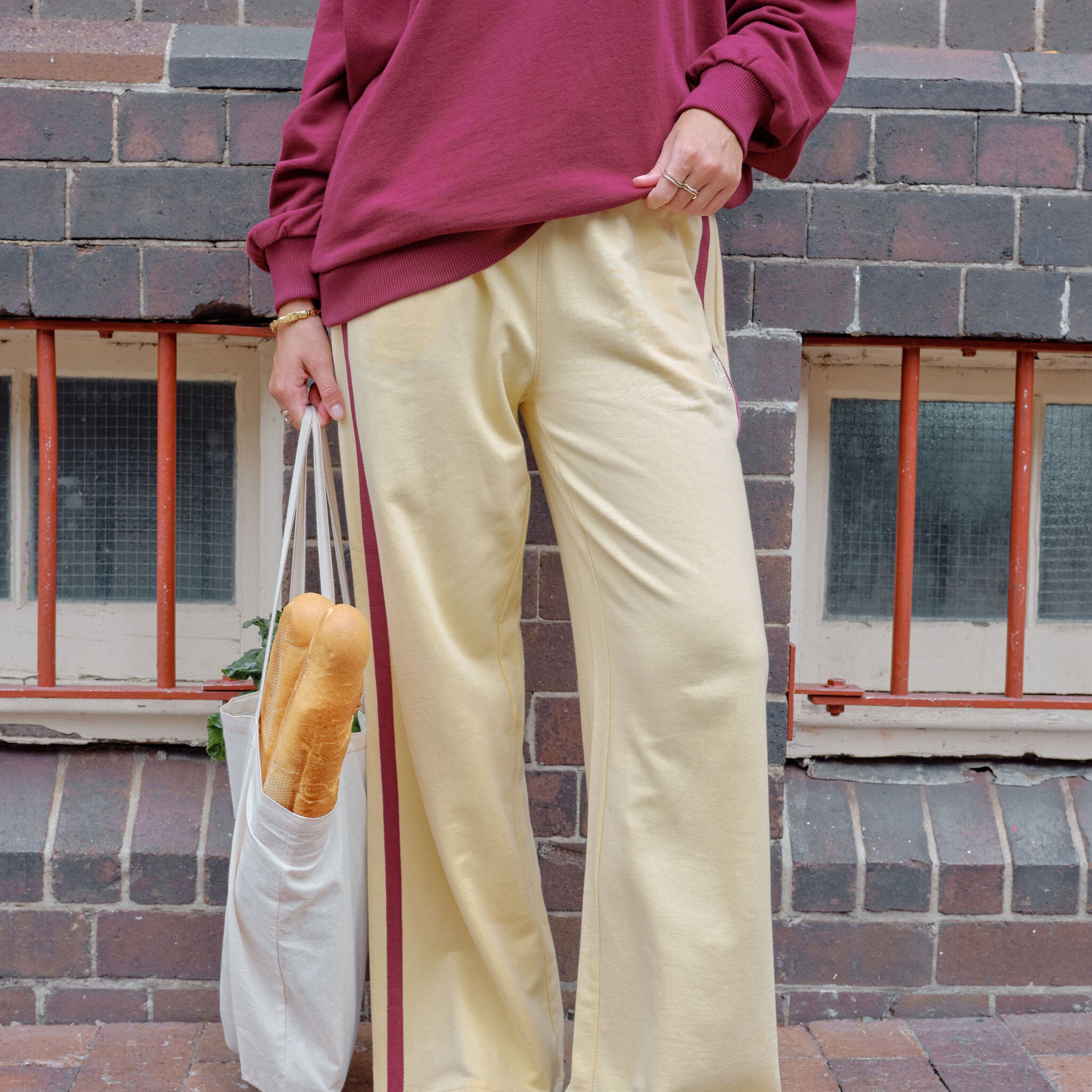 Woman sitting wearing pink wide leg track pants with white side stripe on park bench
