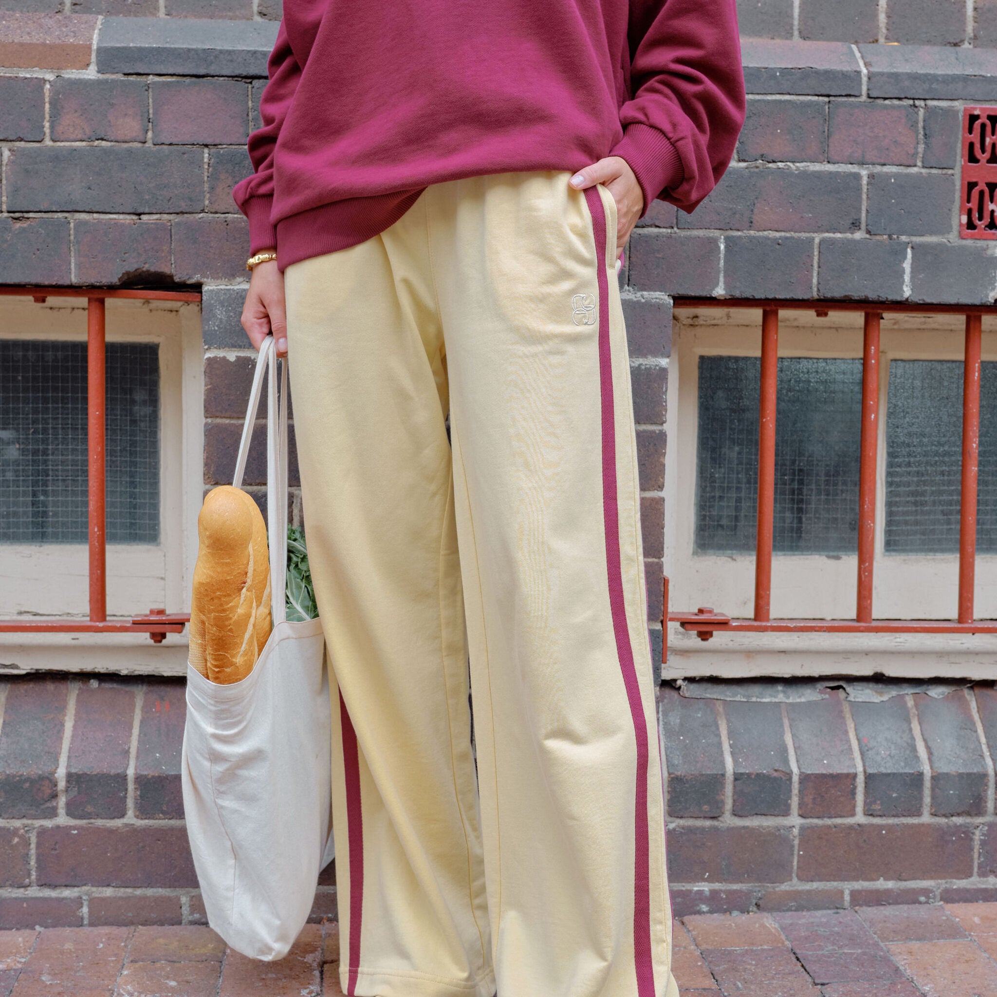Woman wearing cream wide leg track pants with brown side stripe styled with crossbody bag