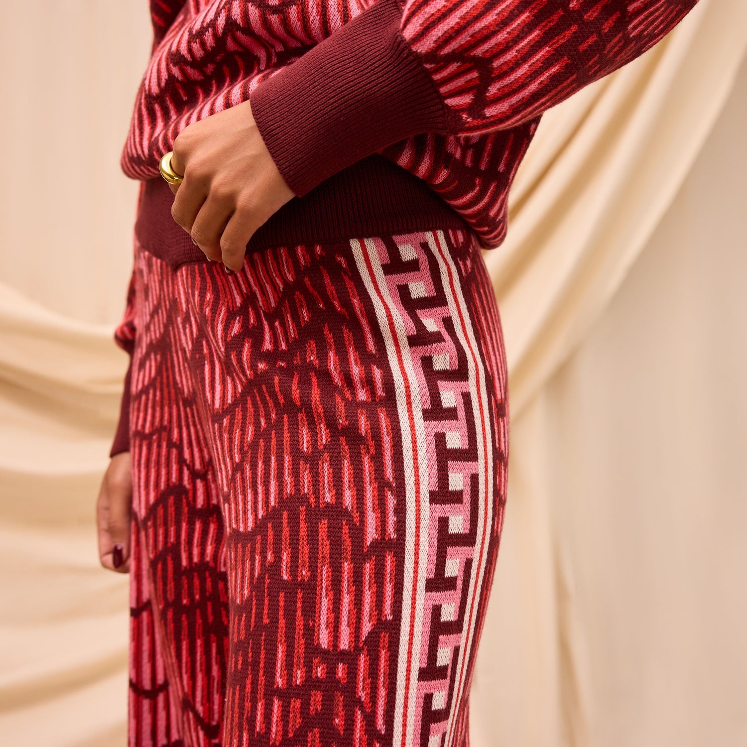 Side detail view of red knit Hanna pants showing Greek key tape trim and textured fabric