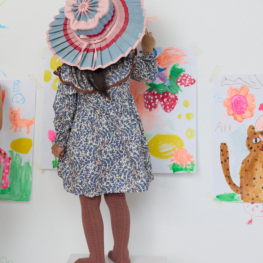 Child wearing Lorna Murray Luxe Capri Hat in Ice Cream colorway with pleated blue pink red ribbon trim