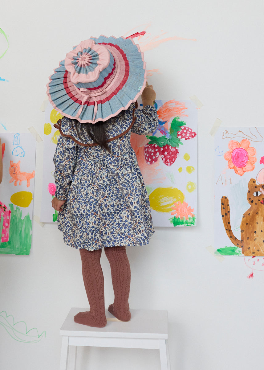 Child wearing Lorna Murray Luxe Capri Hat in Ice Cream colorway with pleated blue pink red ribbon trim