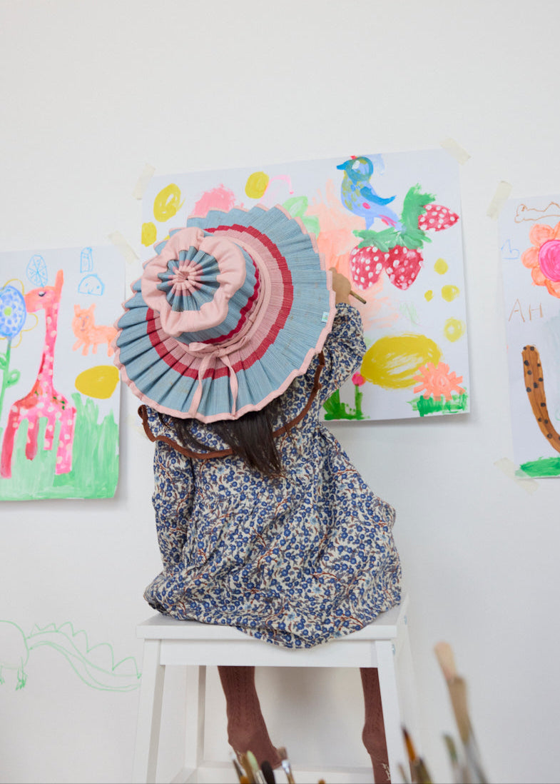 Side lifestyle shot of child in Luxe Capri Hat Ice Cream style sitting against colorful artwork wall