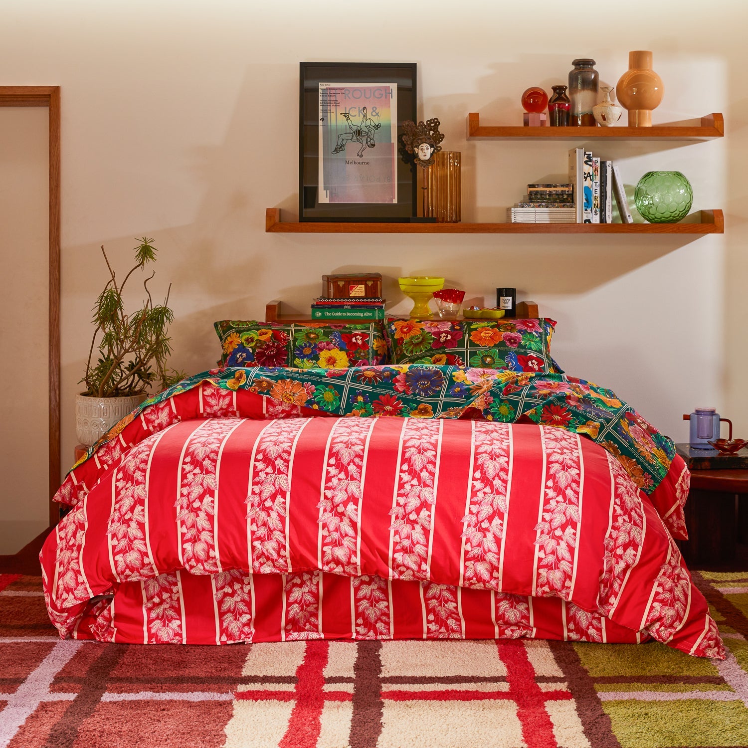 Wide bedroom shot of Ines Silk Pillowcase Verdant styled with red striped sheets and contemporary furniture