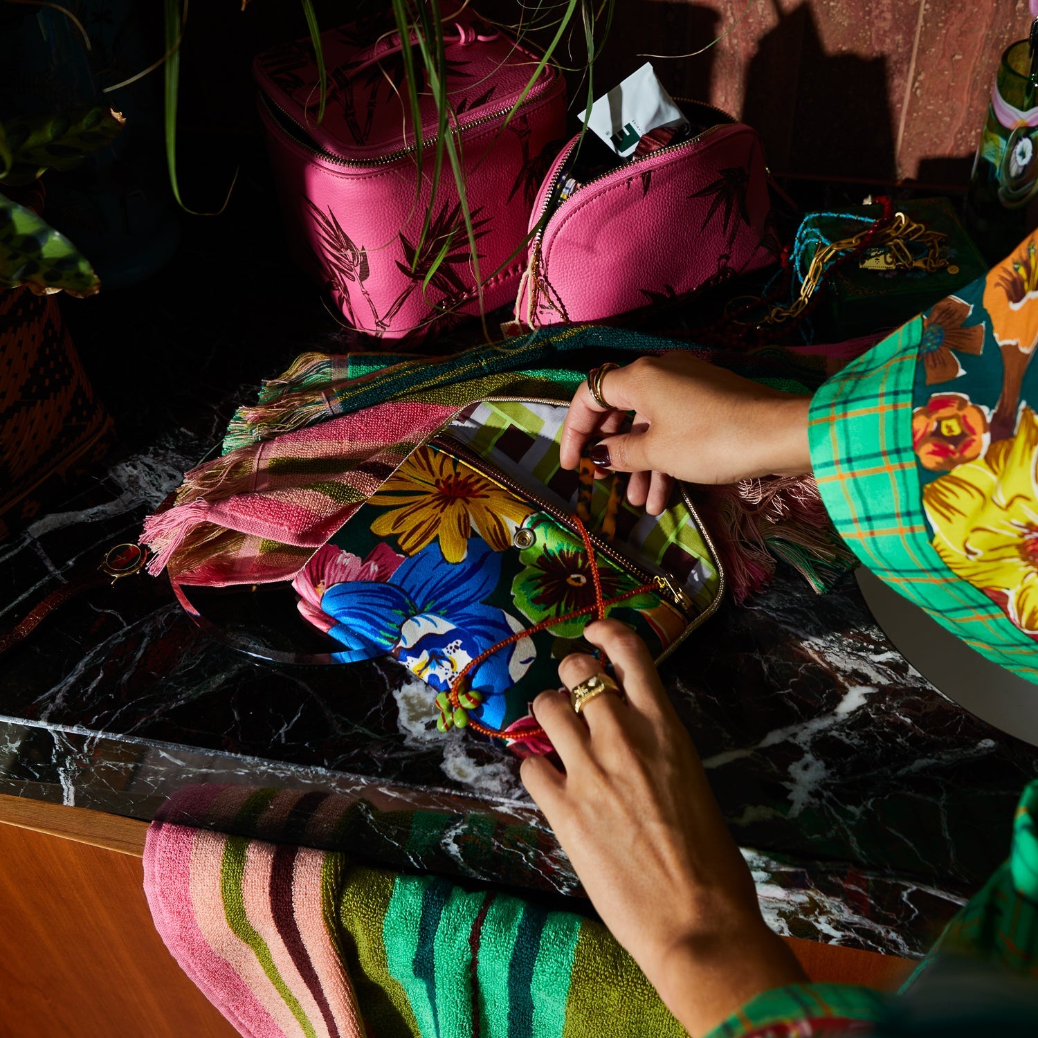 Hands opening silk pouch revealing interior zipper compartment and tropical flower pattern exterior