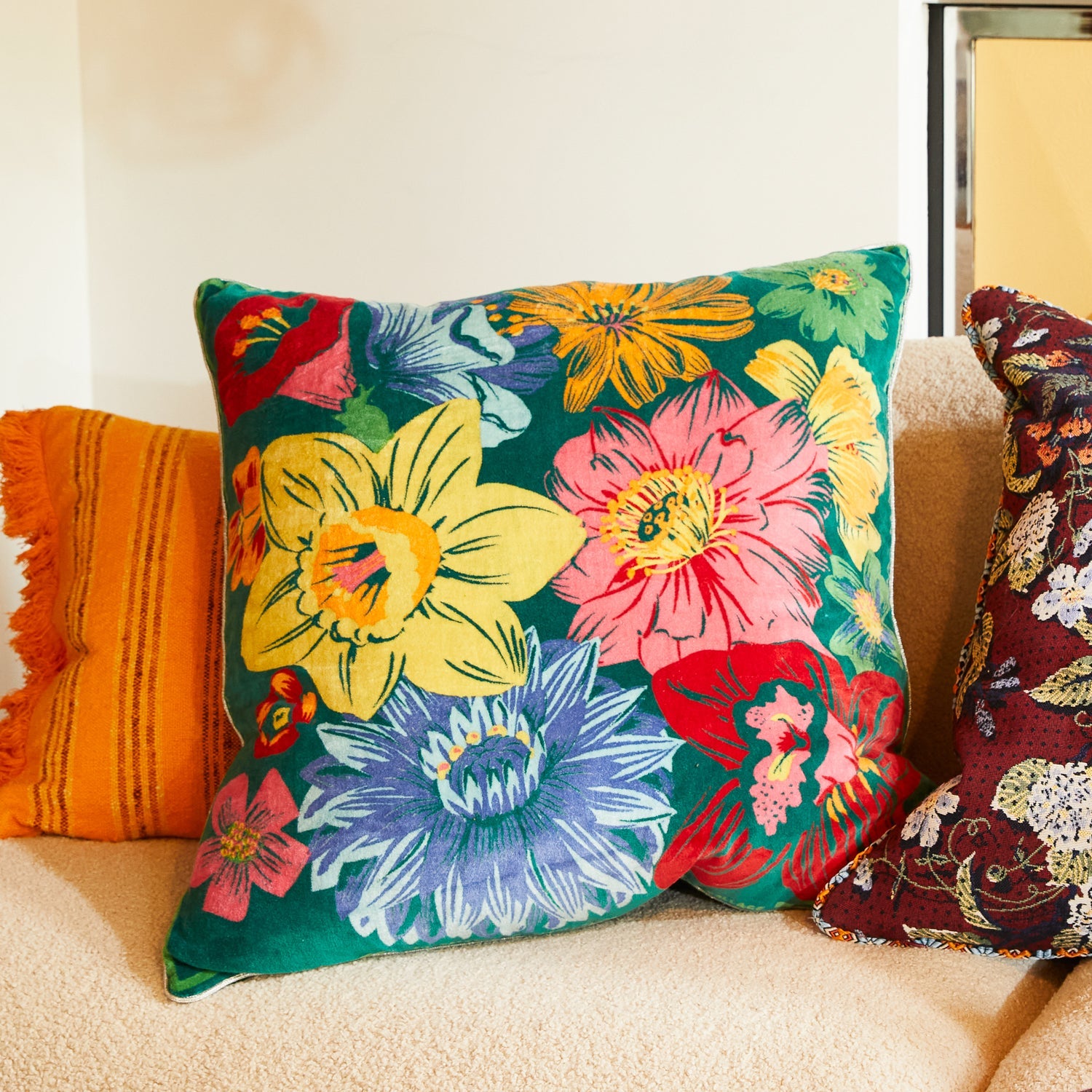Ines Velvet Cushion in Verdant green with vibrant floral pattern styled on beige sofa with orange throw