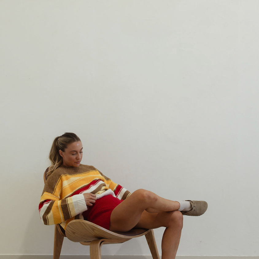 Relaxed pose showing Isabel Knit autumn stripe sweater with oversized fit and long sleeves on seated model