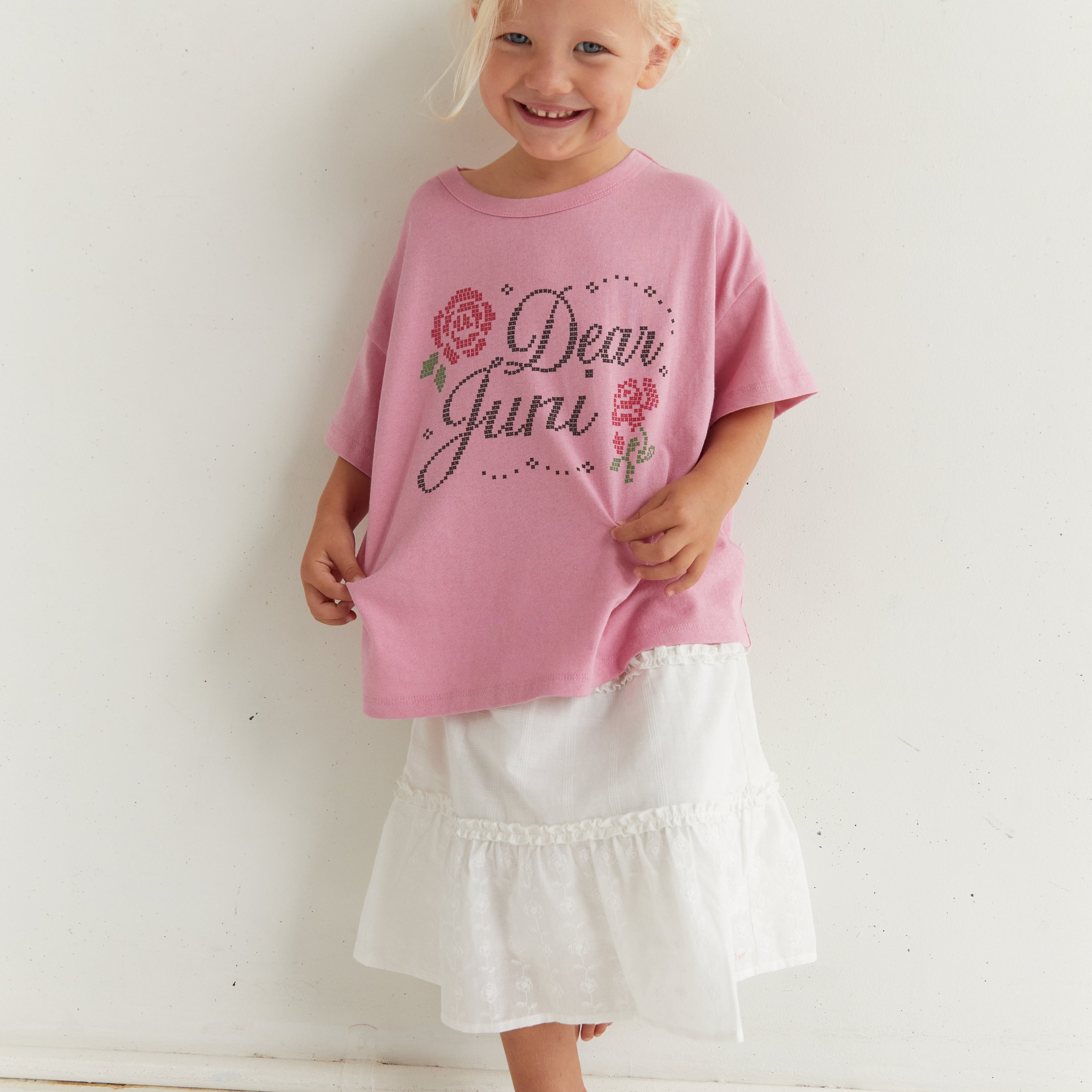 Front view of pink Dear Juni tee on child showing rhinestone lettering and floral design