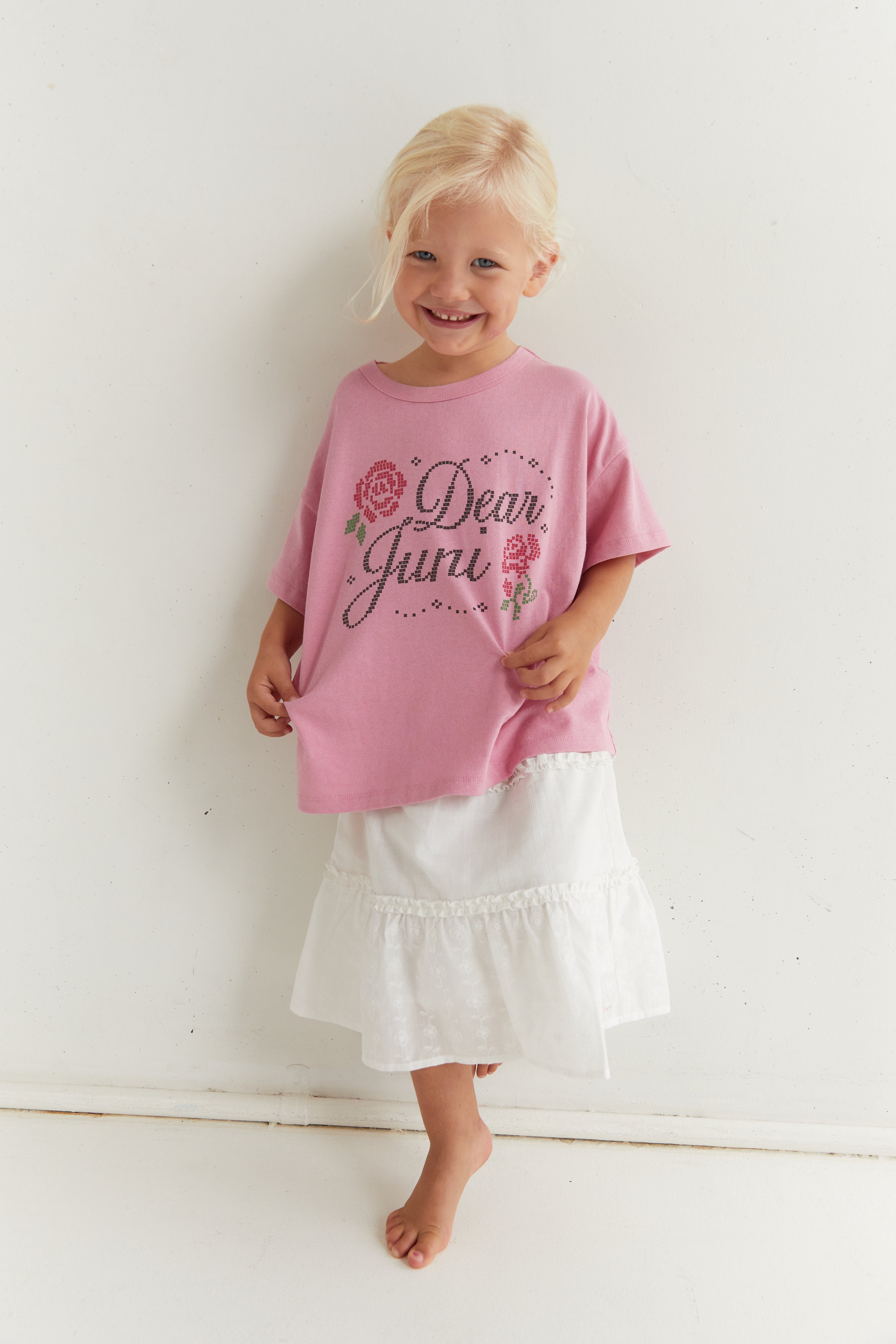Front view of pink Dear Juni tee on child showing rhinestone lettering and floral design