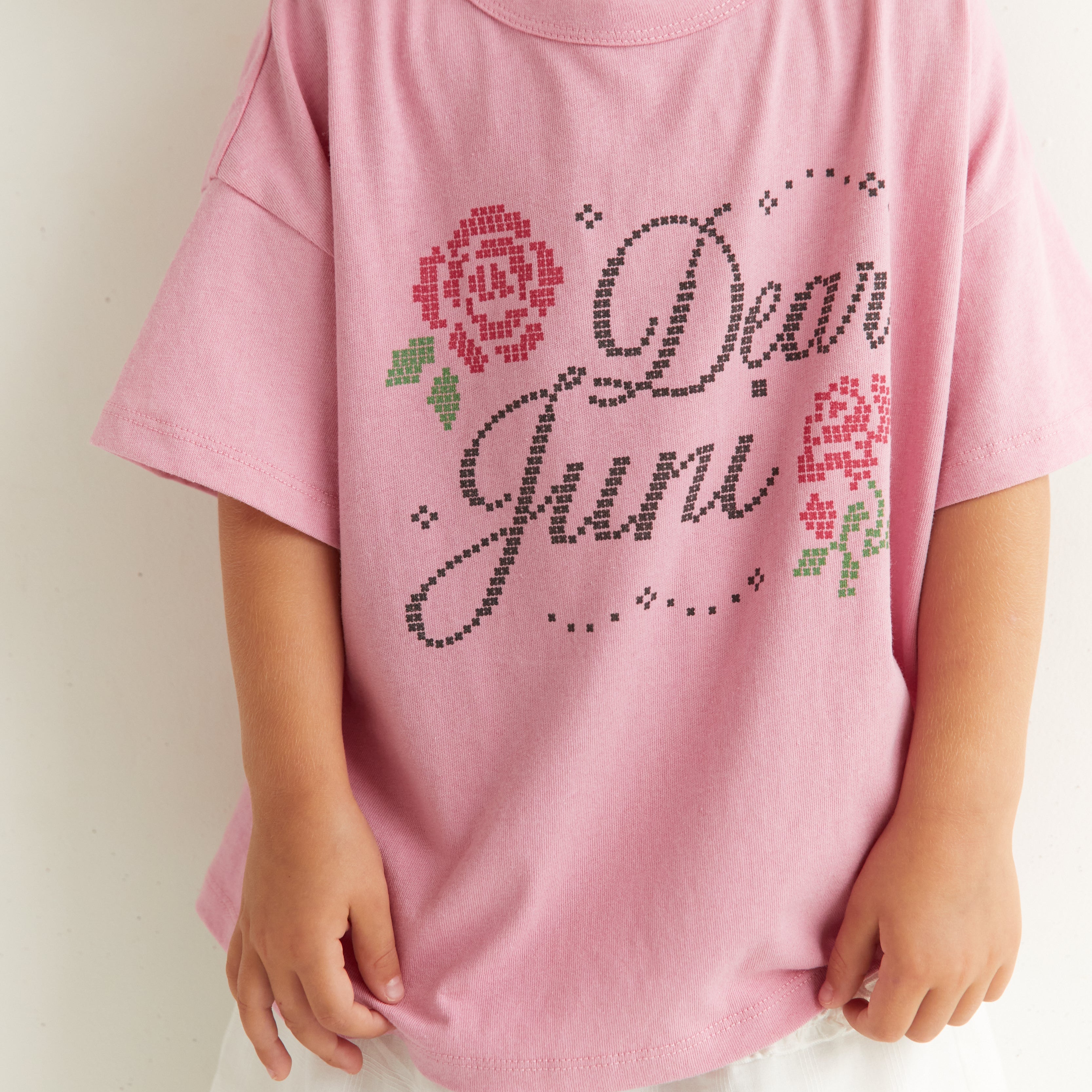 Close-up of Dear Juni tee showing rhinestone text detail and rose motif on pink fabric