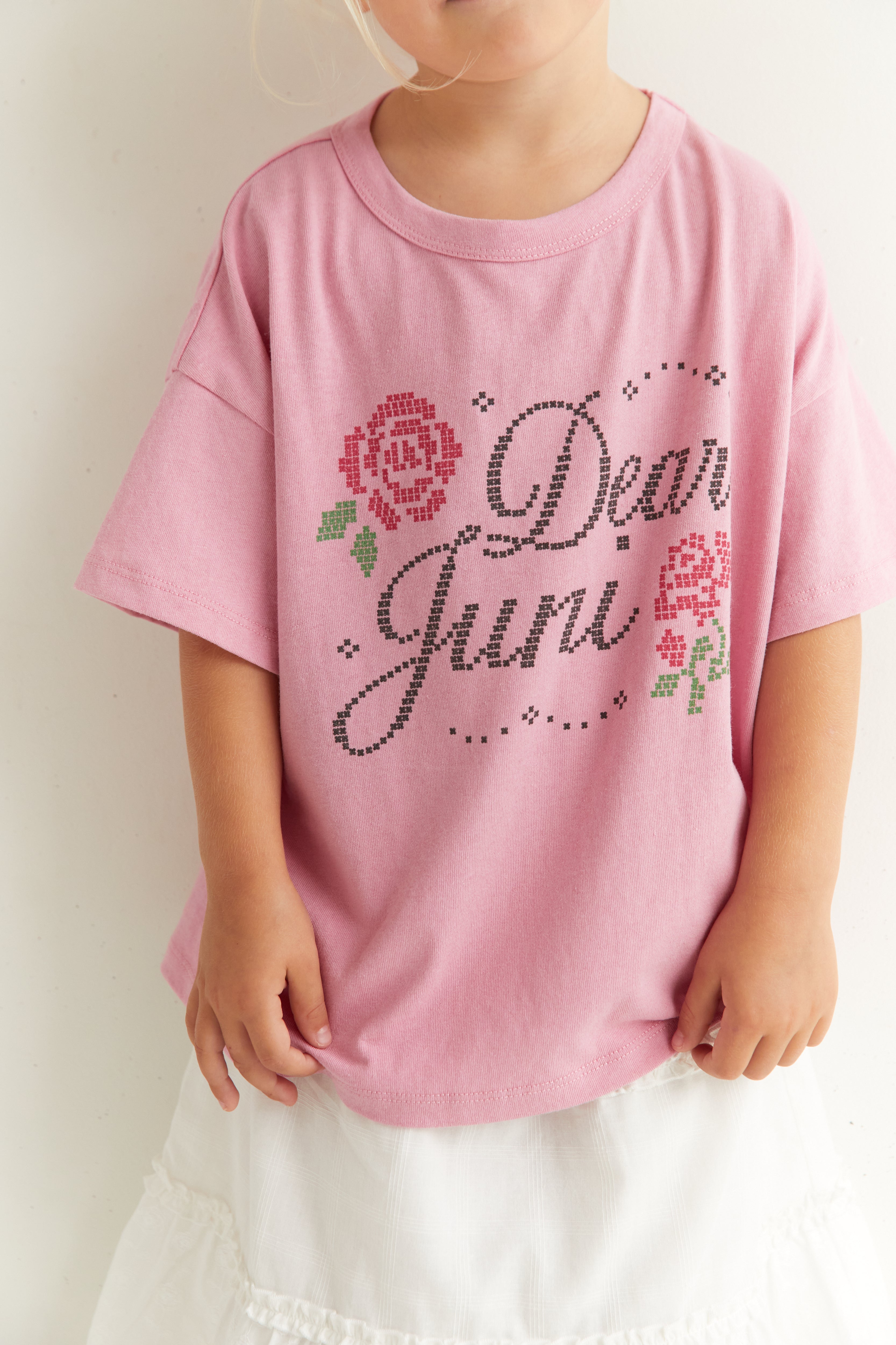 Close-up of Dear Juni tee showing rhinestone text detail and rose motif on pink fabric