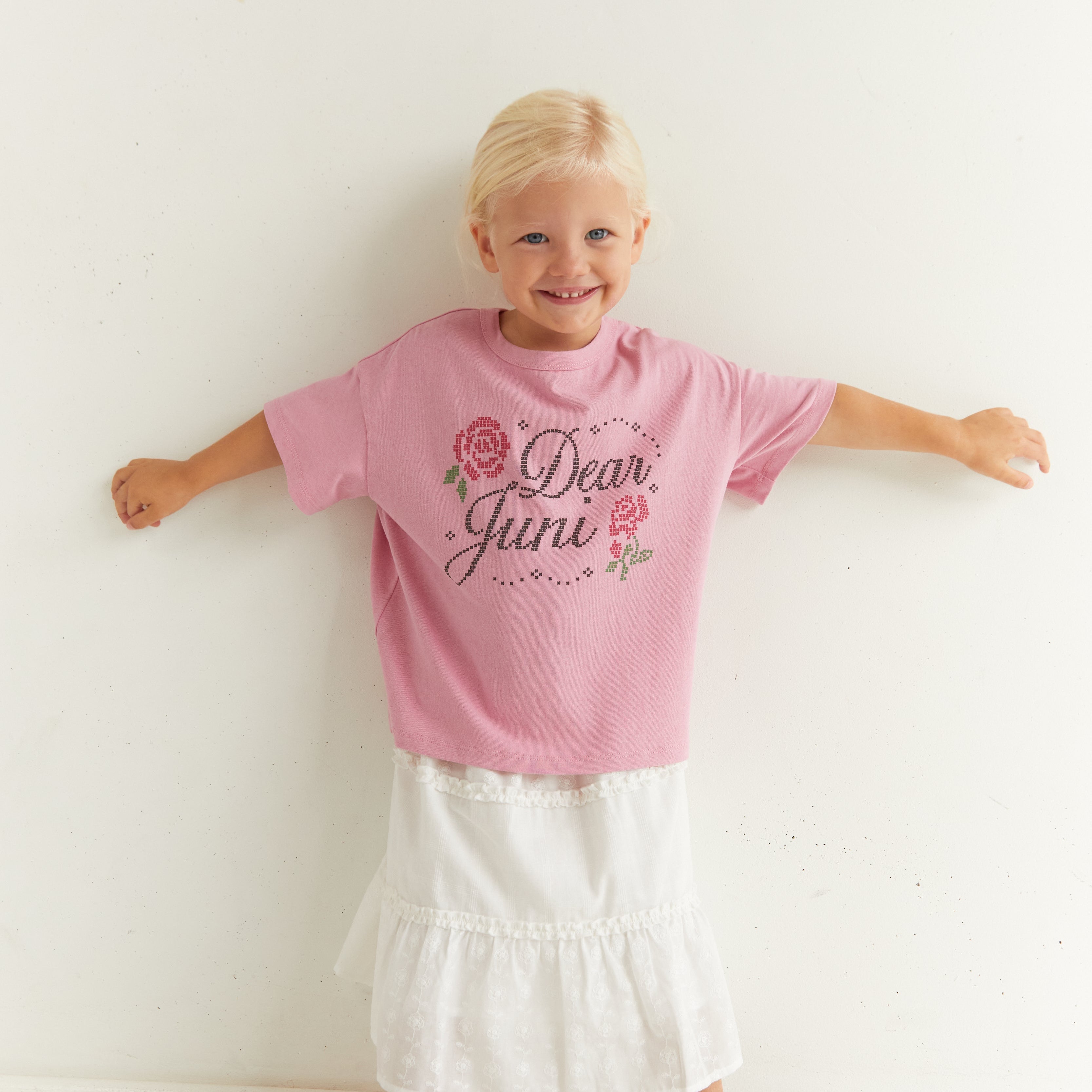 Full front view of child in pink Dear Juni tee with arms outstretched showing fit and design