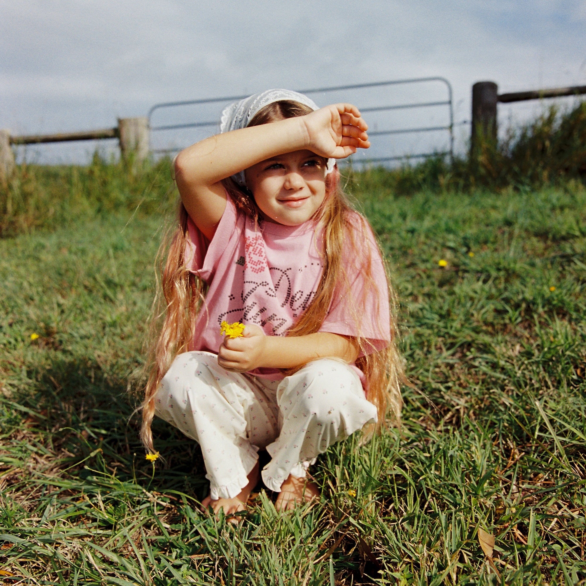 Child sitting outdoors wearing pink Dear Juni tee with rhinestone graphics in natural setting