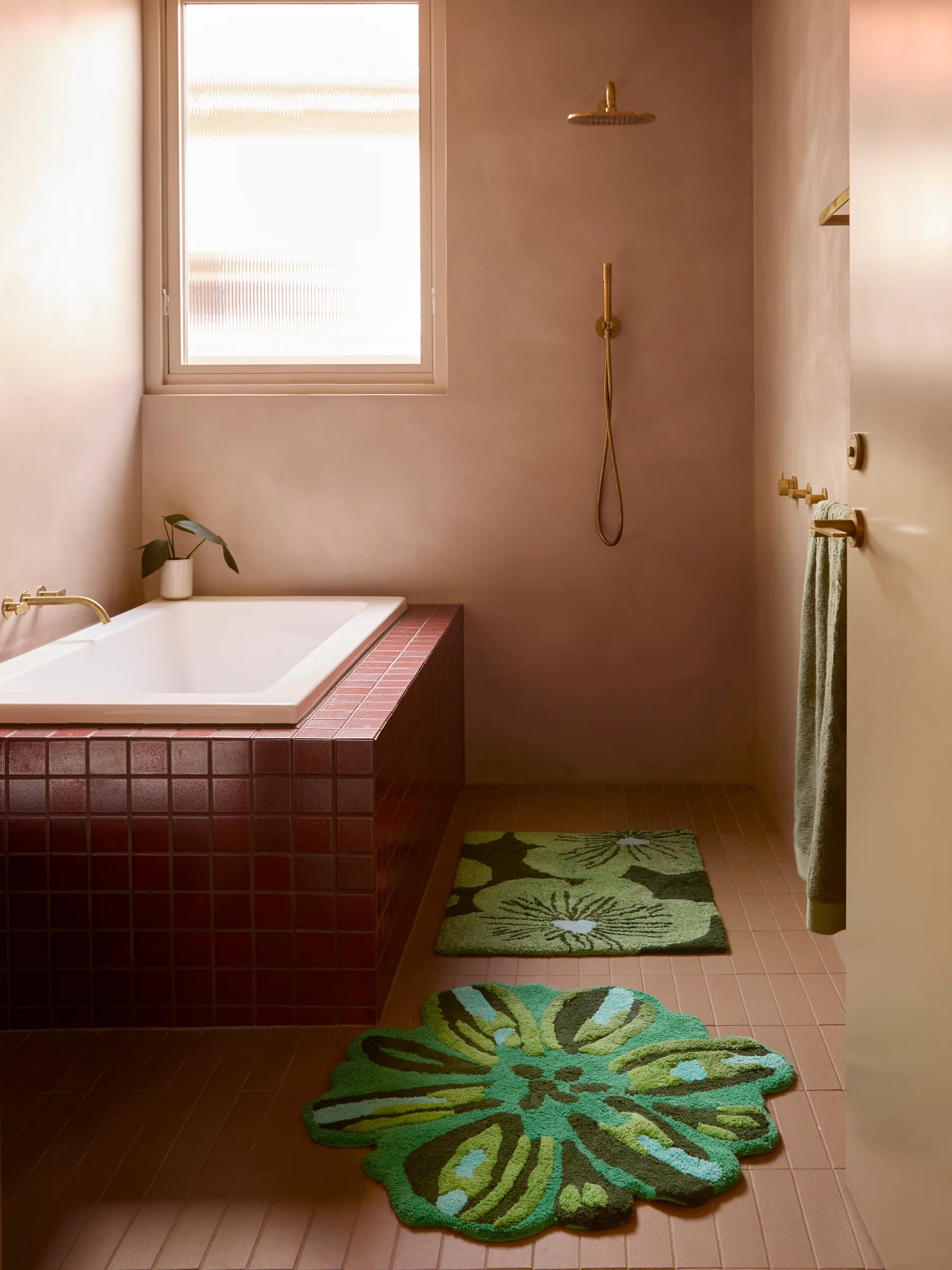Jardin green bath mat by Bonnie and Neil displayed in a pink rendered bath room with a red tiled bath