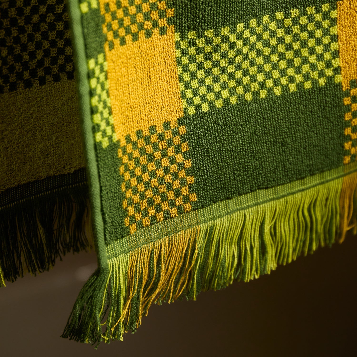 Close-up of the fringed hem and green and yellow plaid woven terry fabric of a hand towel