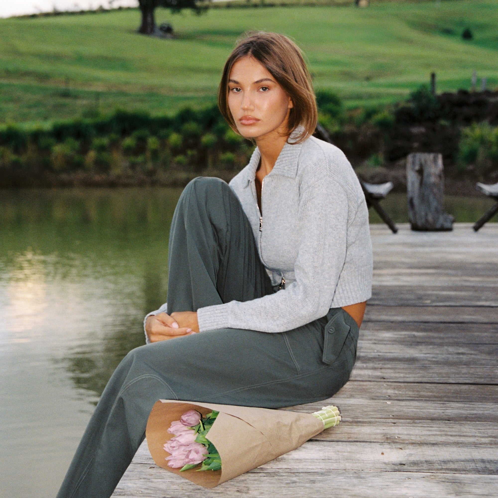 Side angle of stone knit Kaia Zip Cardigan with collar and cropped fit on wooden dock