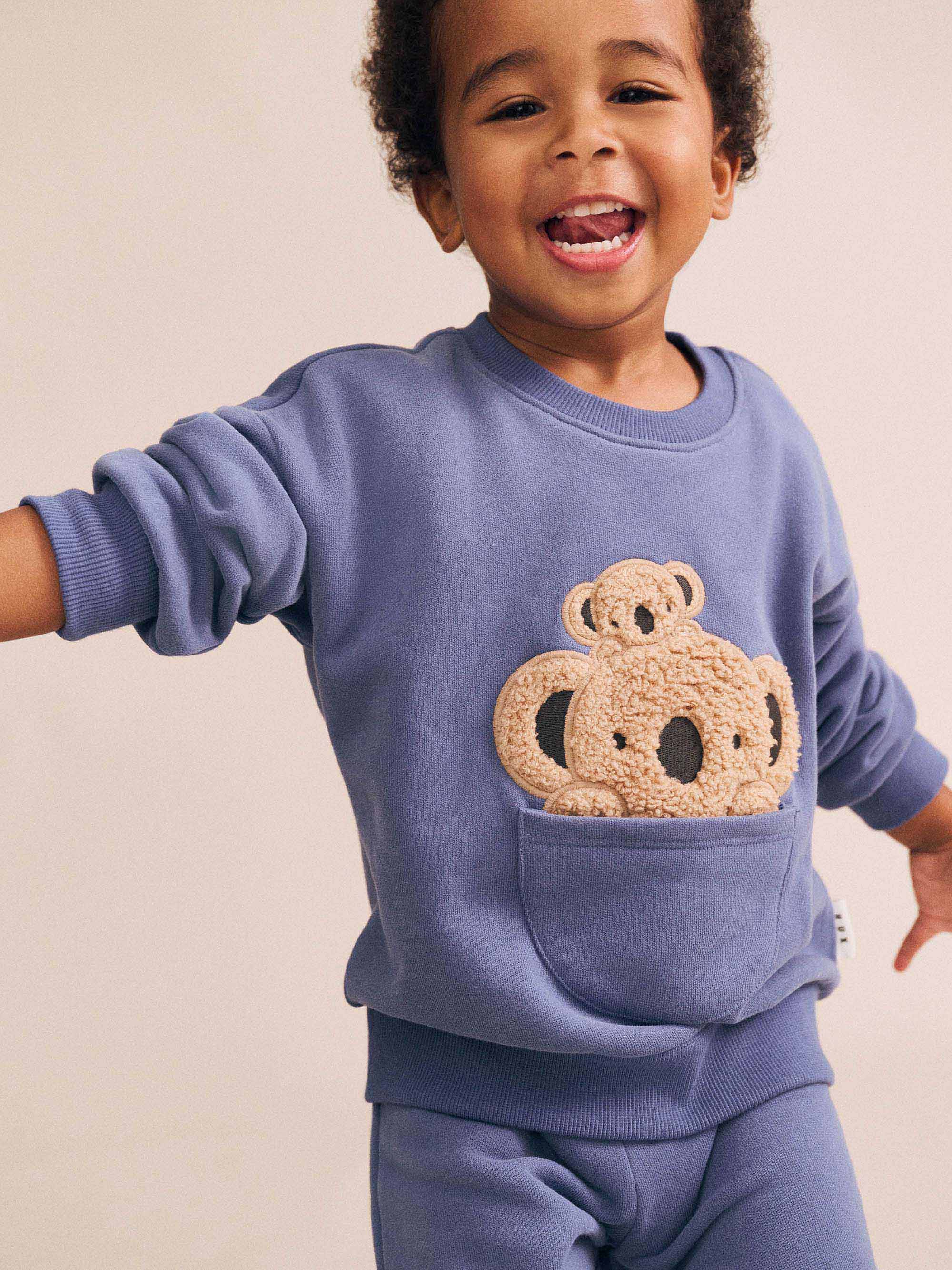 Child wearing matching blue Huxbaby koala sweatshirt with Kel Koala Trackpant set showing coordinated outfit