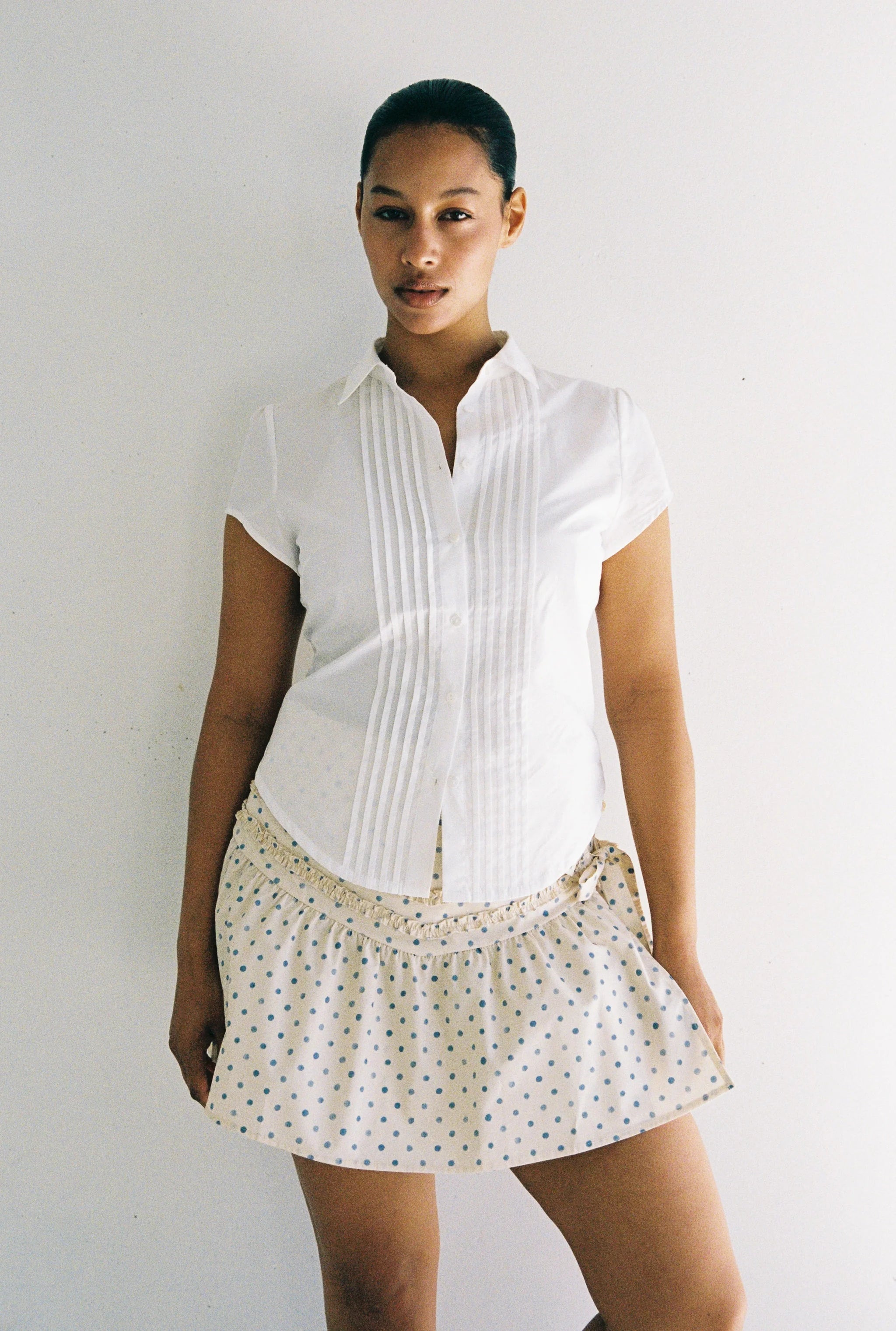 Woman wearing a white blouse and polka dot skirt against a plain background